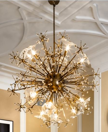 A modern chandelier with a starburst design, featuring multiple branches with small bulbs and glass decorative elements, hanging from a high ceiling.