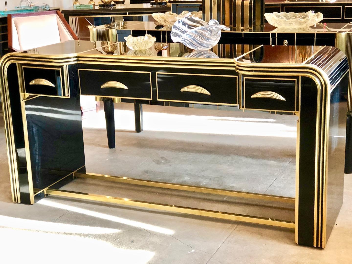 Black and gold console table with three drawers, decorated with glass sculptures on top, in an interior setting.