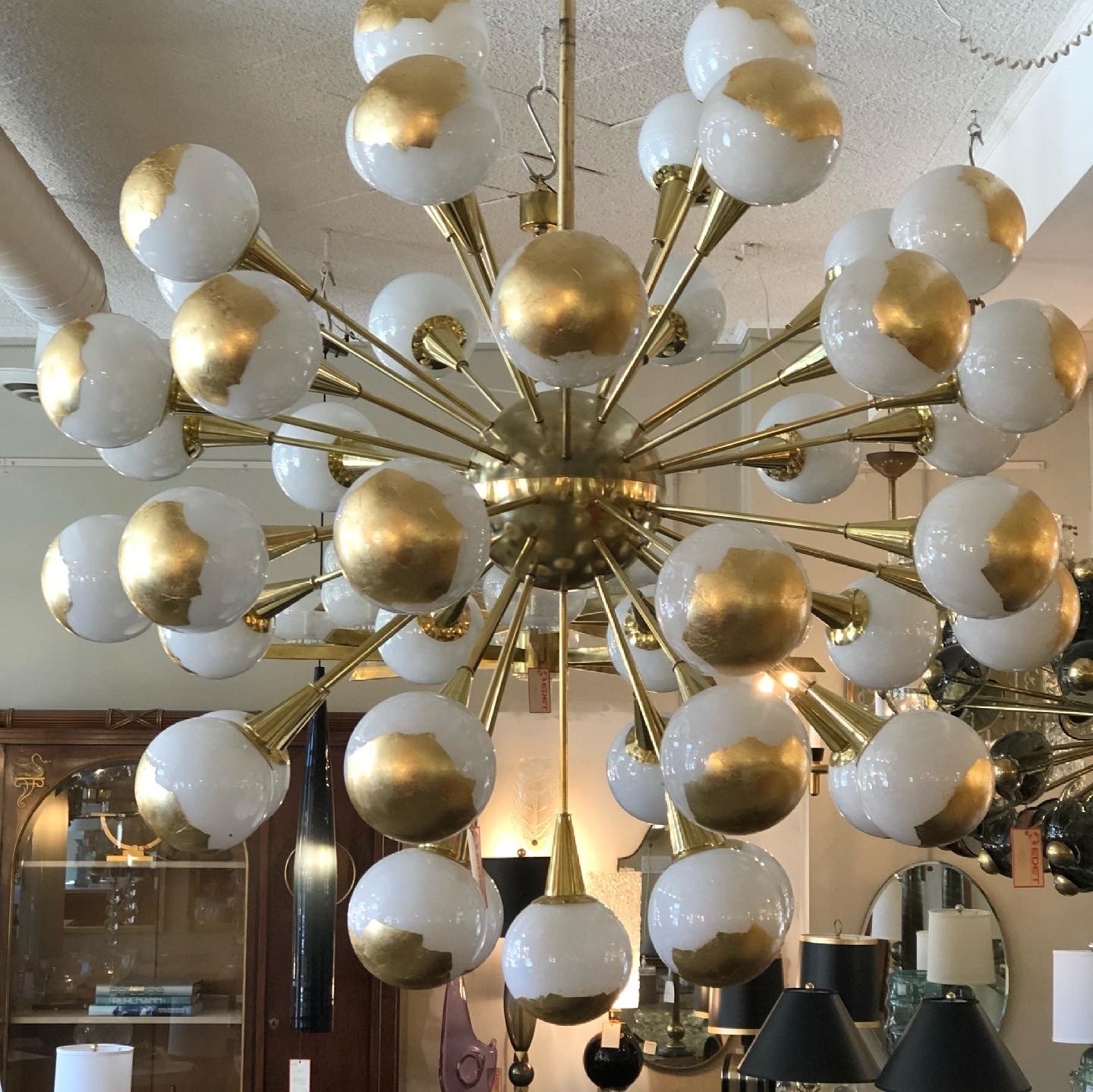 A gold and white sputnik chandelier with multiple globe lights hanging from a ceiling in an interior space.