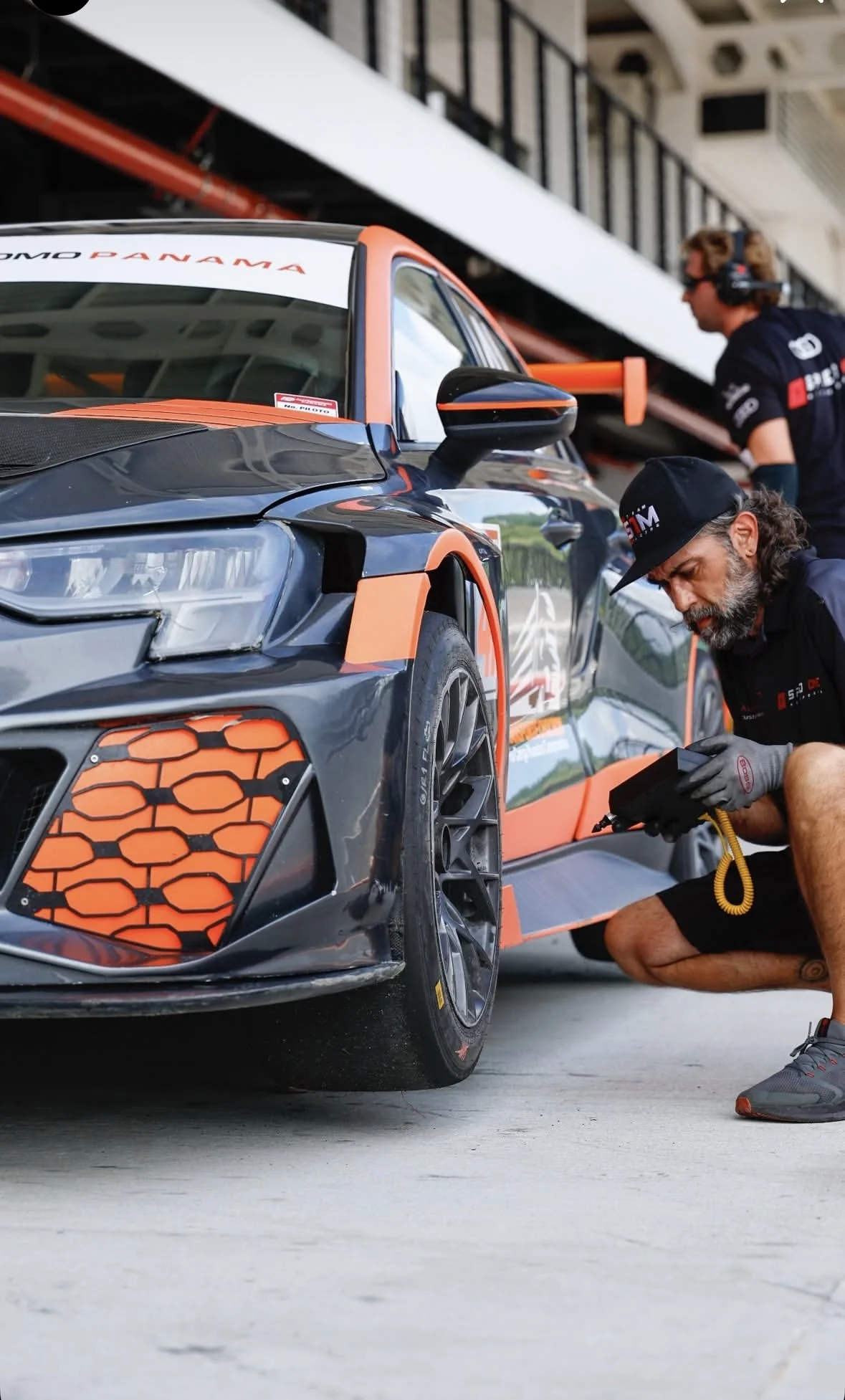 Race car in a pit stop with mechanics working on it, featuring black and orange design elements.