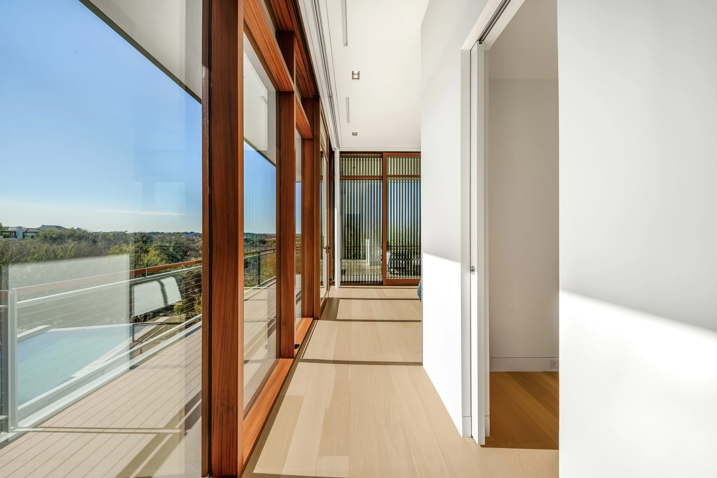 Bright modern living space with large glass sliding doors framed by wood, overlooking a balcony and outdoor landscape.