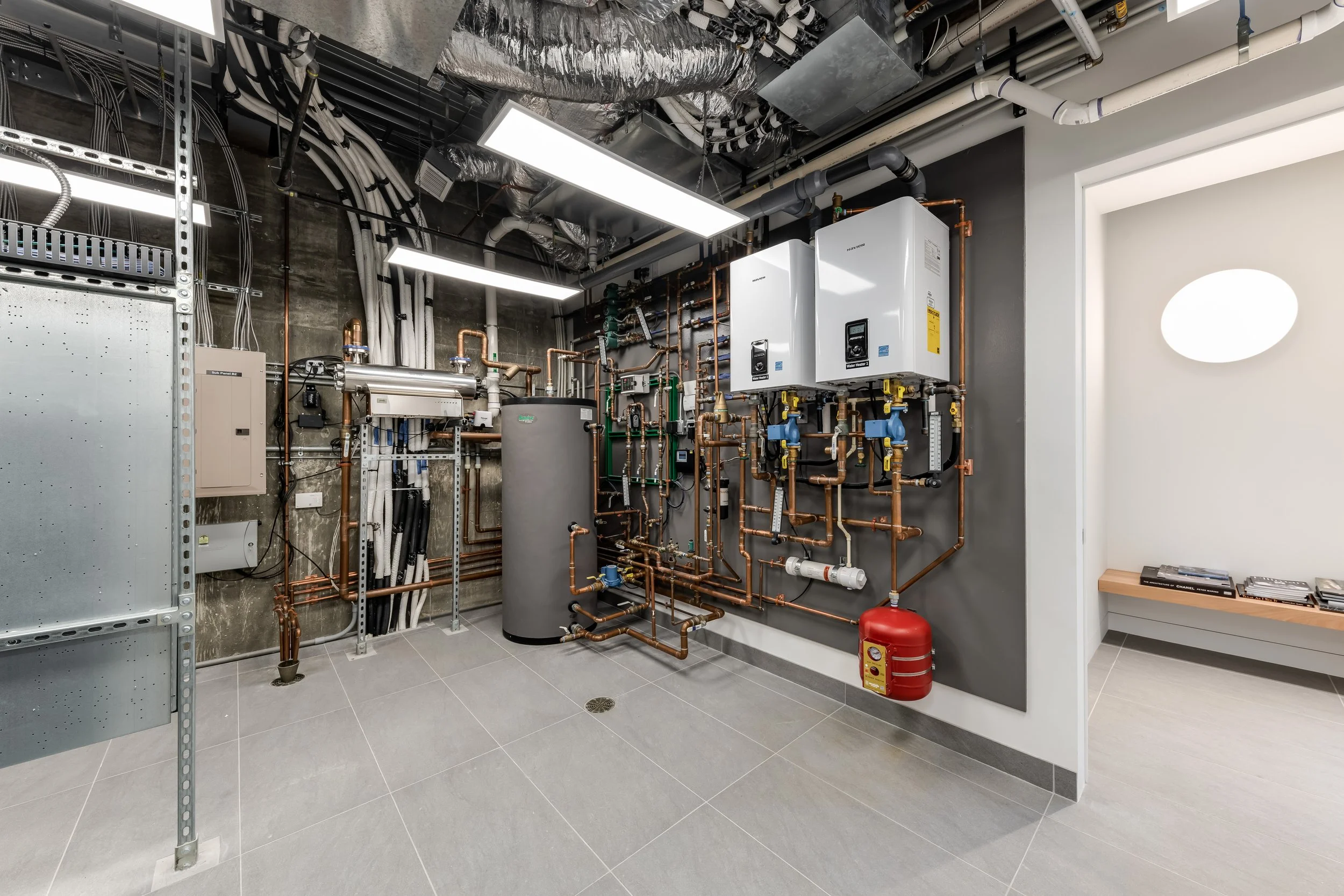 A mechanical room with copper pipes, water heating units, and an electrical panel.