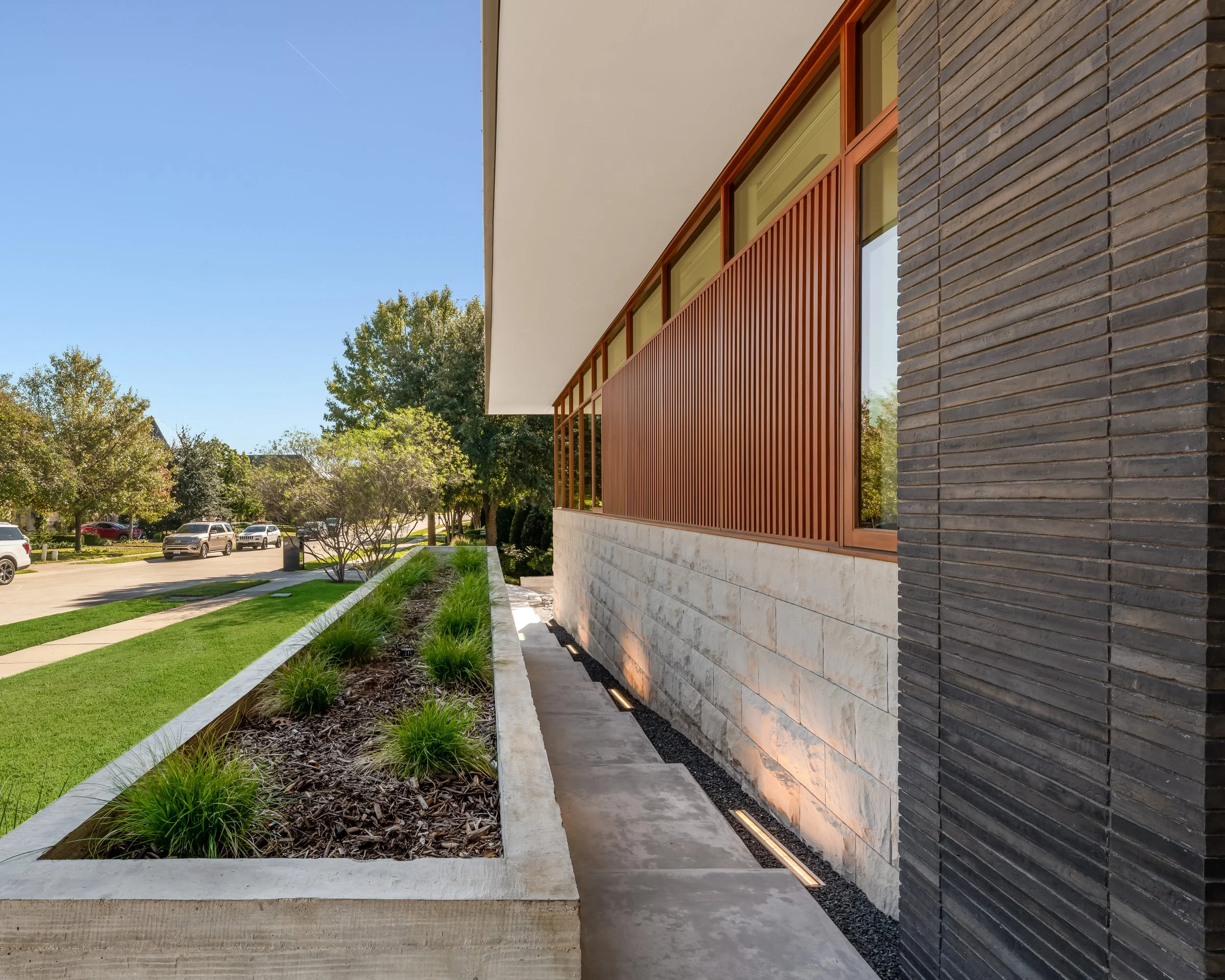 Side view of a modern house with a landscaped garden, brick and wood exterior, and large windows under a clear blue sky.