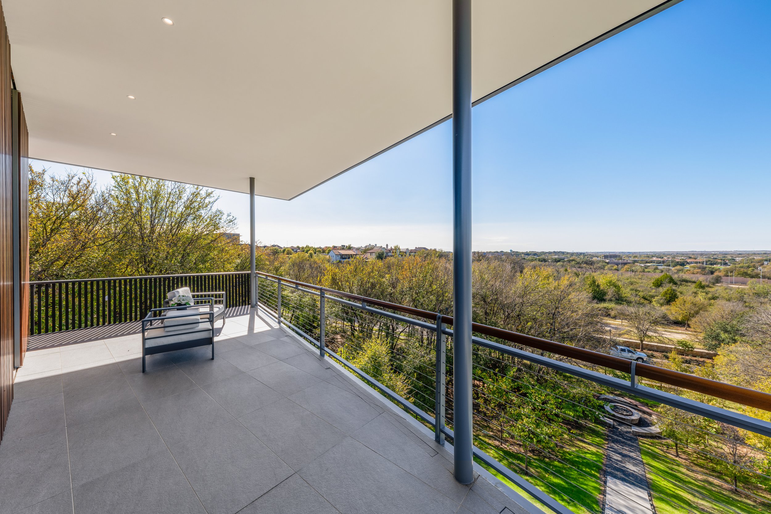 Balcony with two chairs overlooking a green landscape with trees and a distant horizon, under a white ceiling with built-in lights.