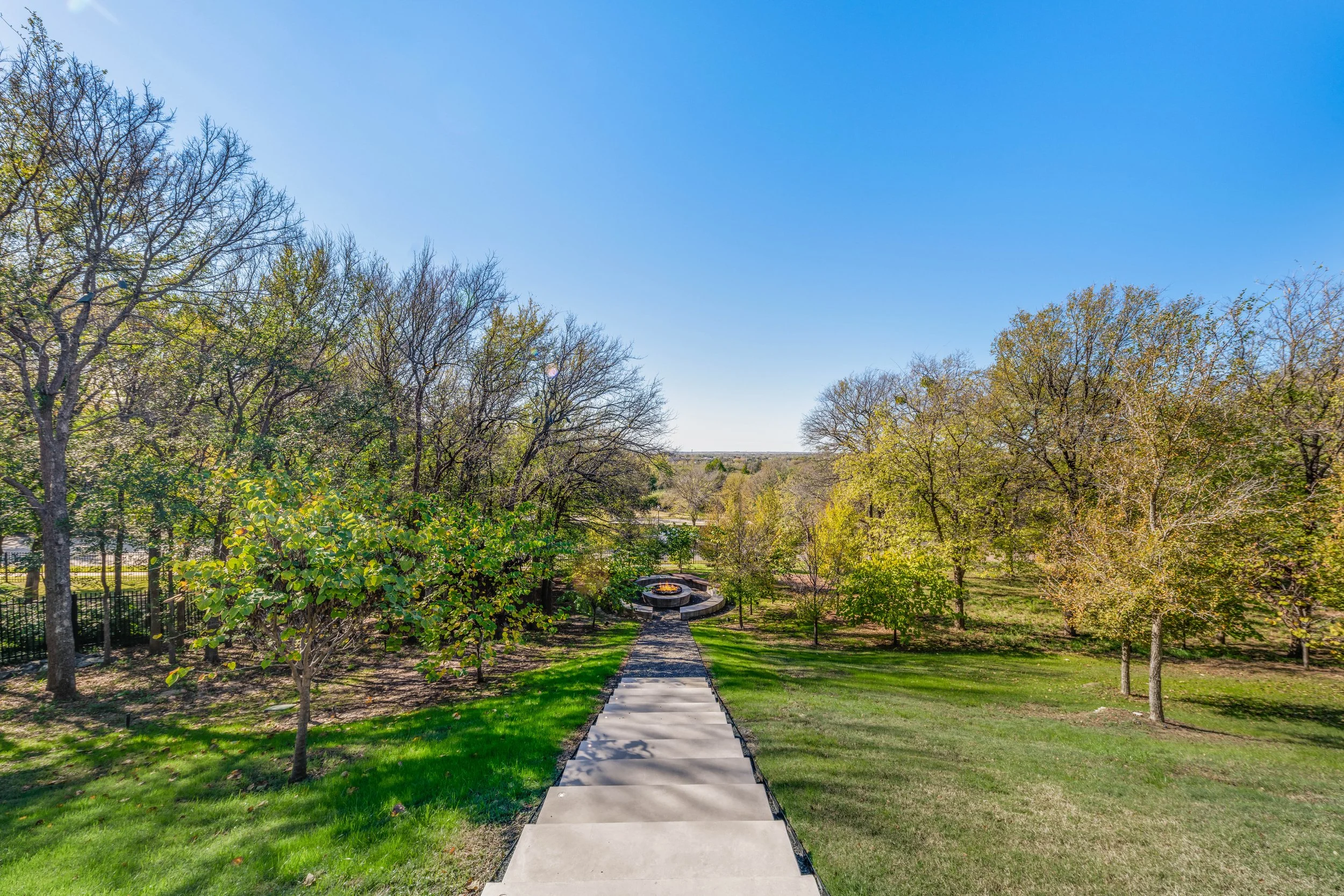 A sidewalk leading to a circular monument in a park with trees and green grass on a sunny day under a clear blue sky.