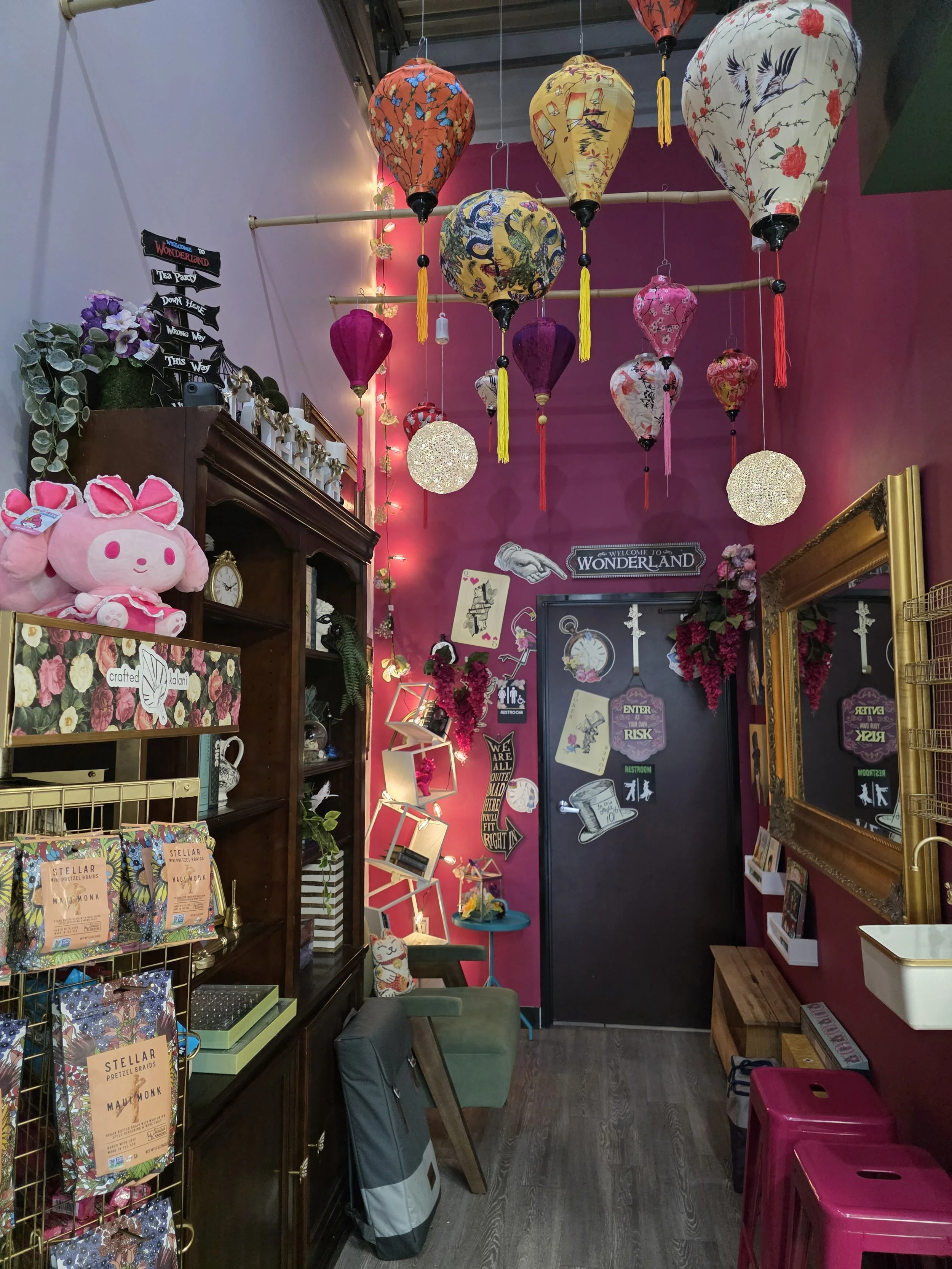 Colorful paper lanterns hanging from the ceiling in a pink-walled boutique or cafe with eclectic decor and assorted merchandise.