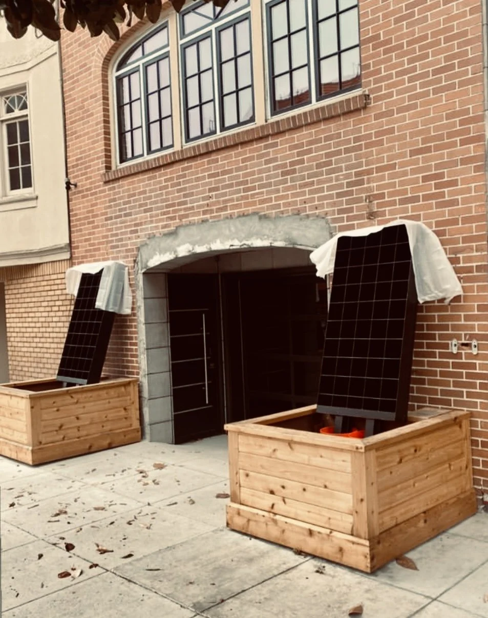 Two wooden planters with solar panels leaning against a brick building entrance under construction.