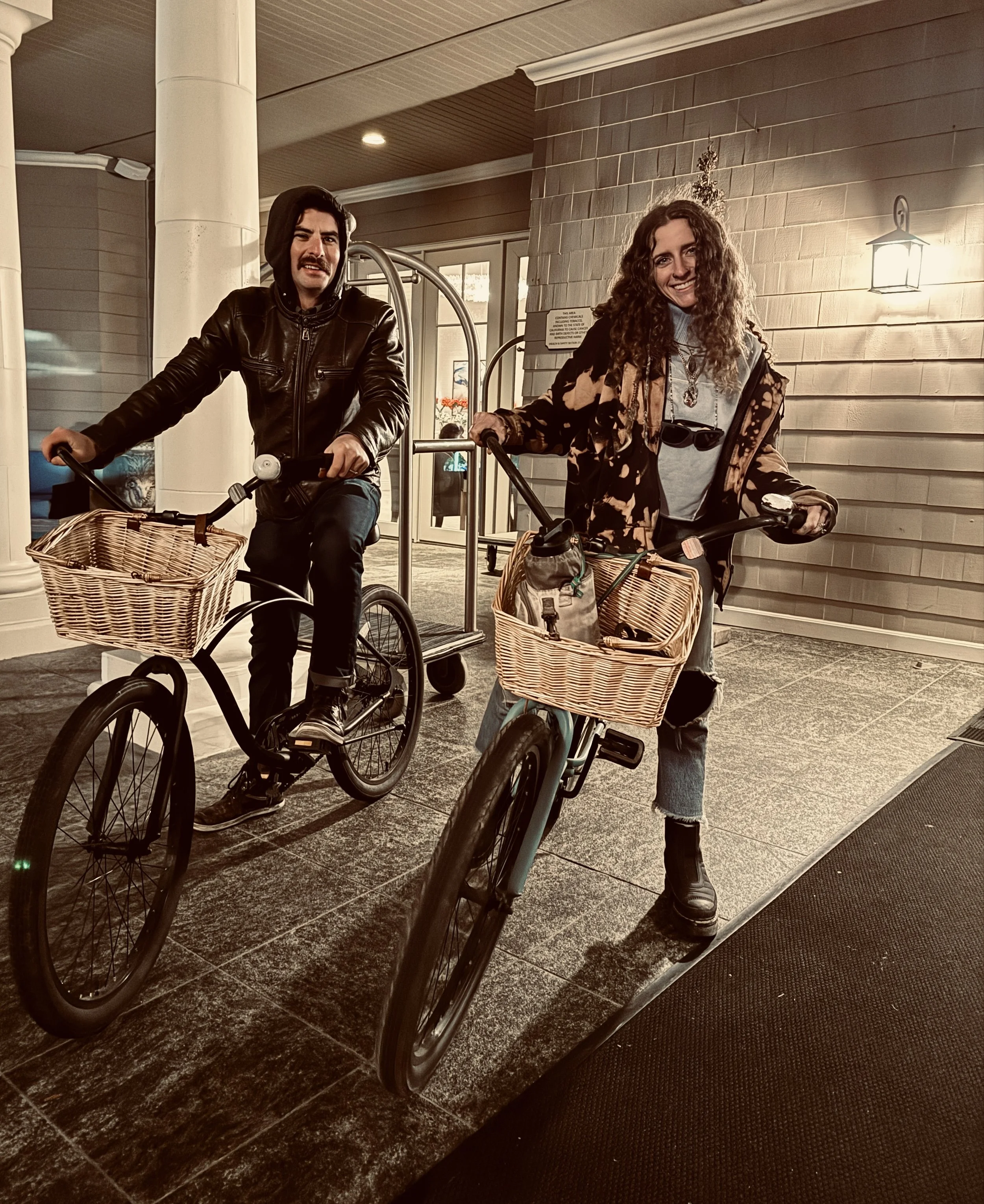 Two people with bicycles standing at the entrance of a building, smiling at the camera.