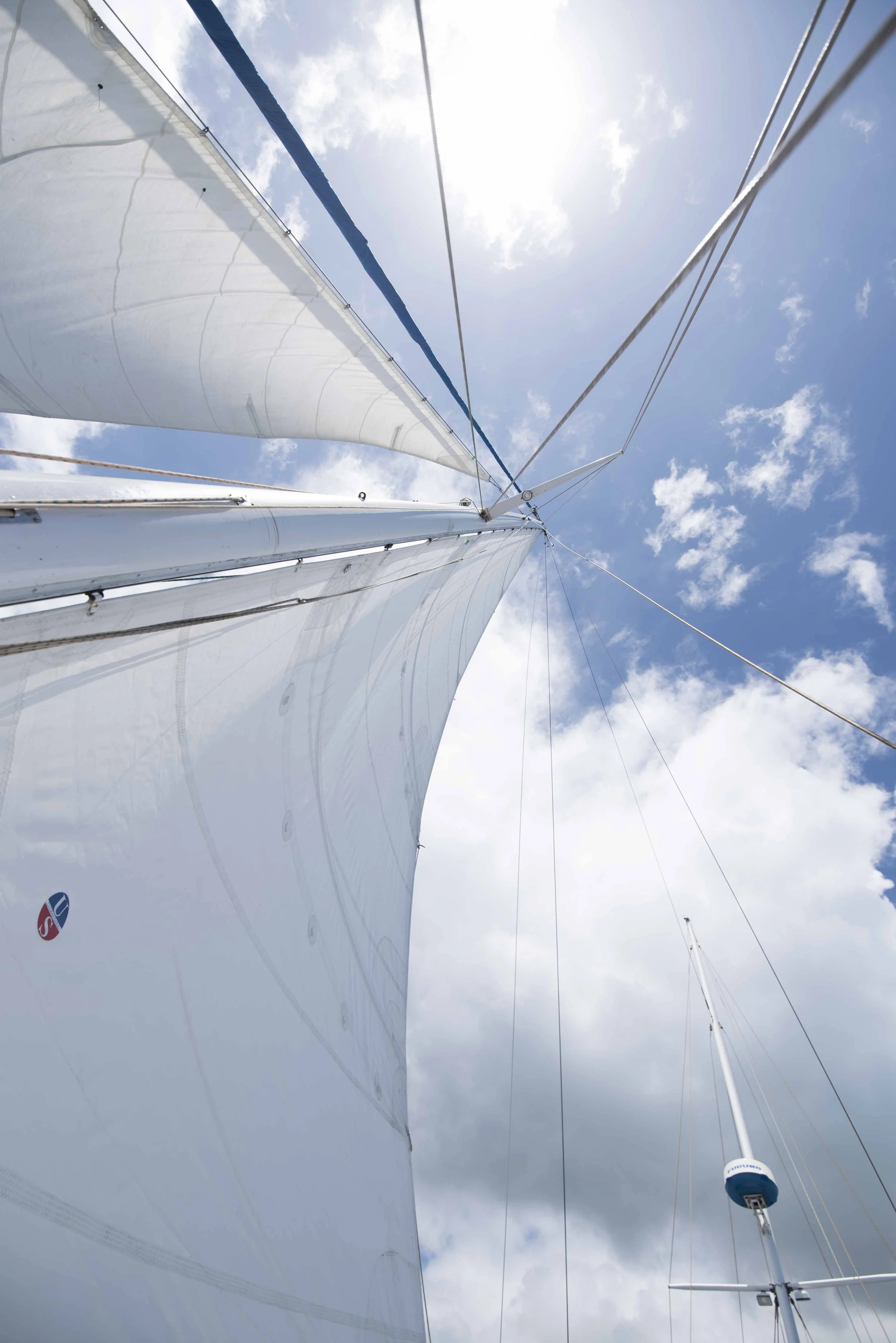 Sailing in Hawaii. Looking up at sailboat masts and sails against a blue sky with scattered clouds.