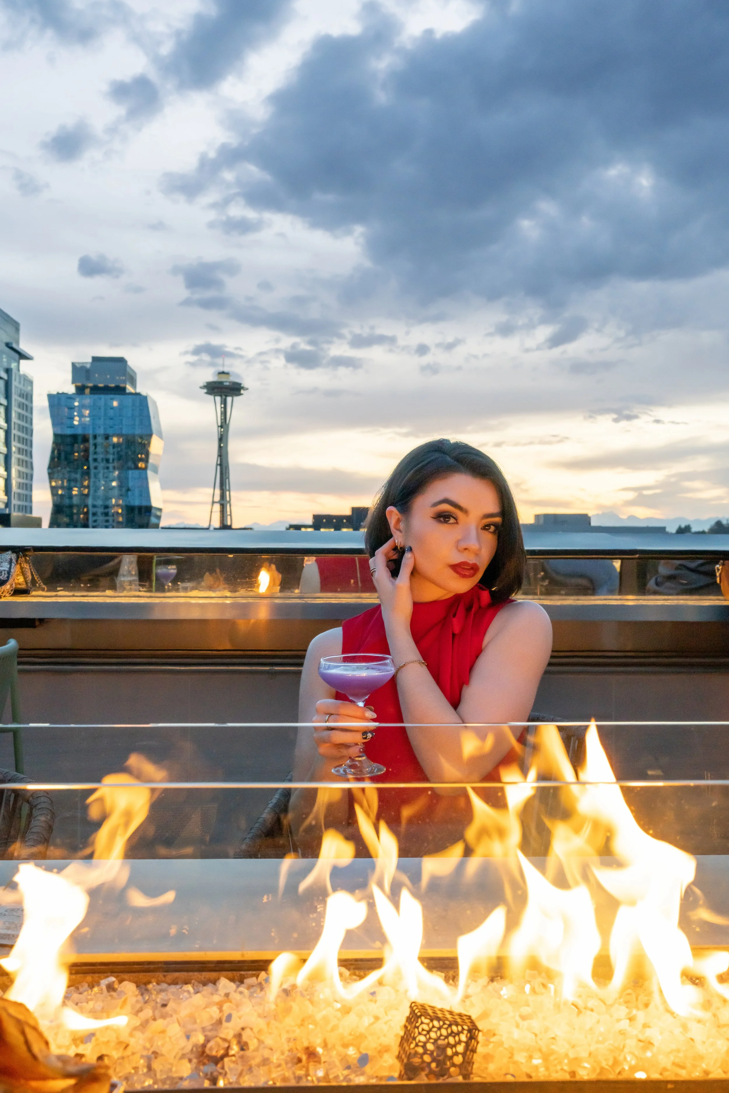 Woman holding cocktail at rooftop fire pit with Space Needle view, Seattle Washington