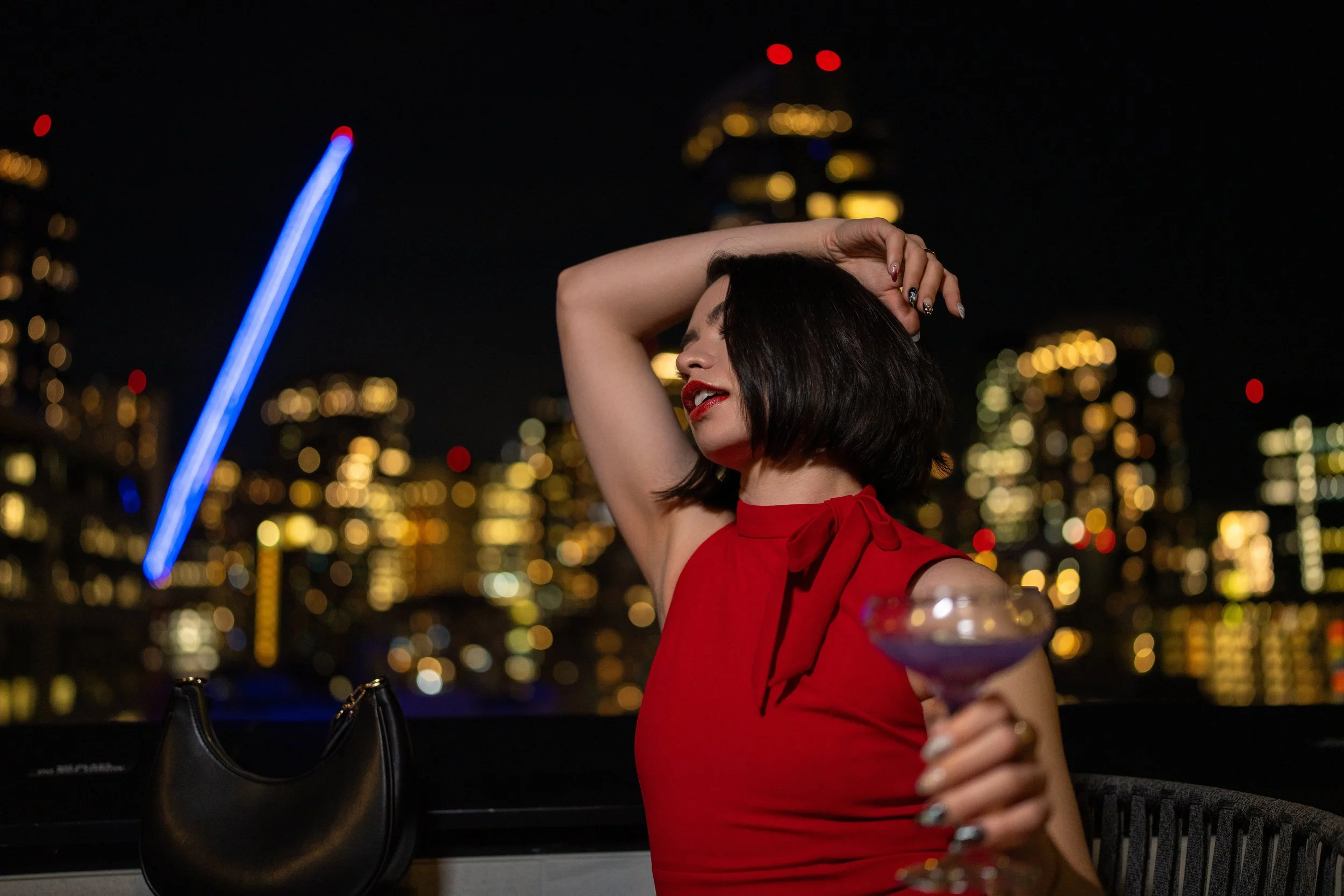 Woman holding cocktail on rooftop with Seattle city lights at night