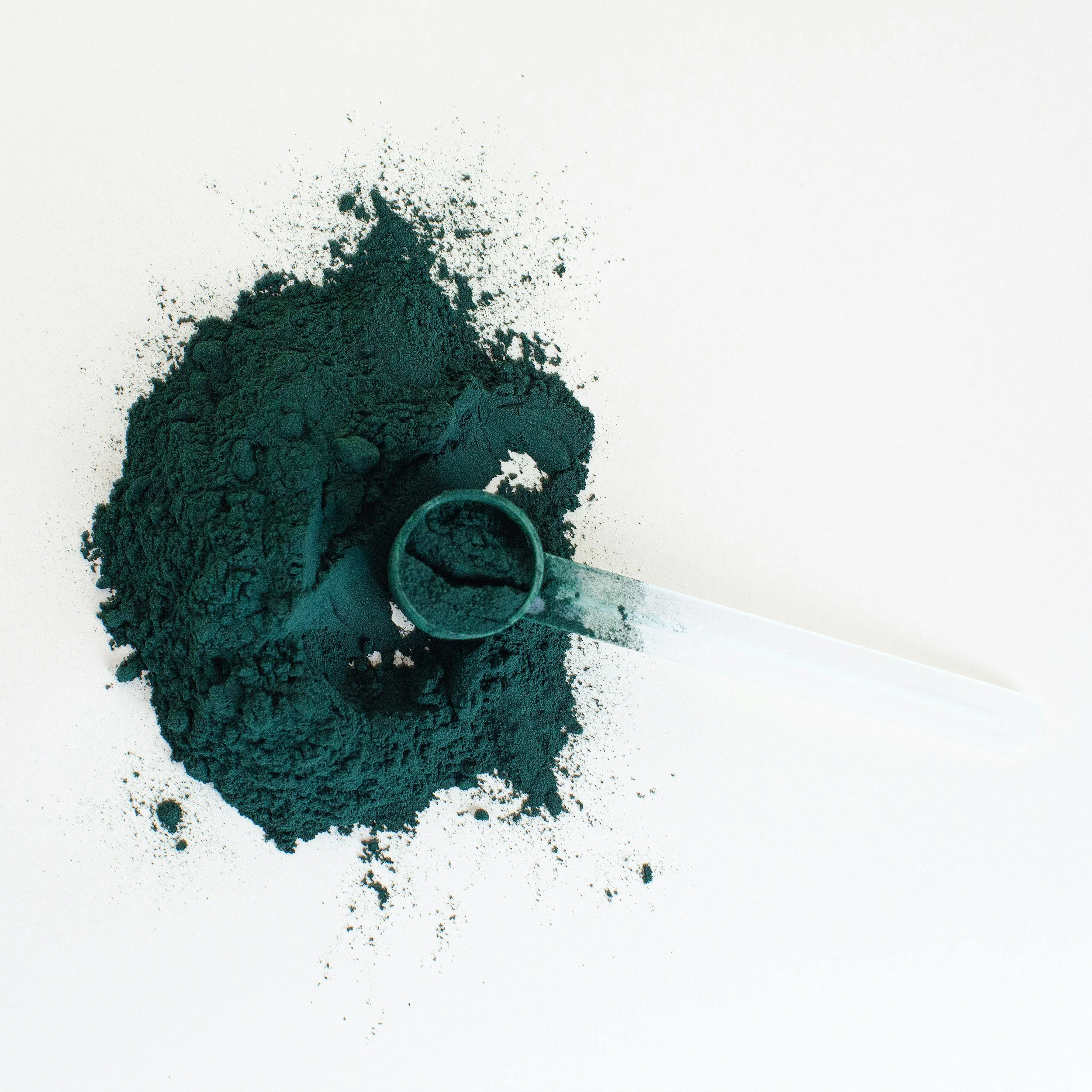 Black powder pigment with a clear glass mixing spoon on a white background.