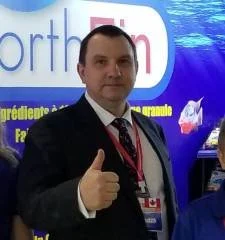 Man in a suit giving a thumbs-up at an event with a blue background.