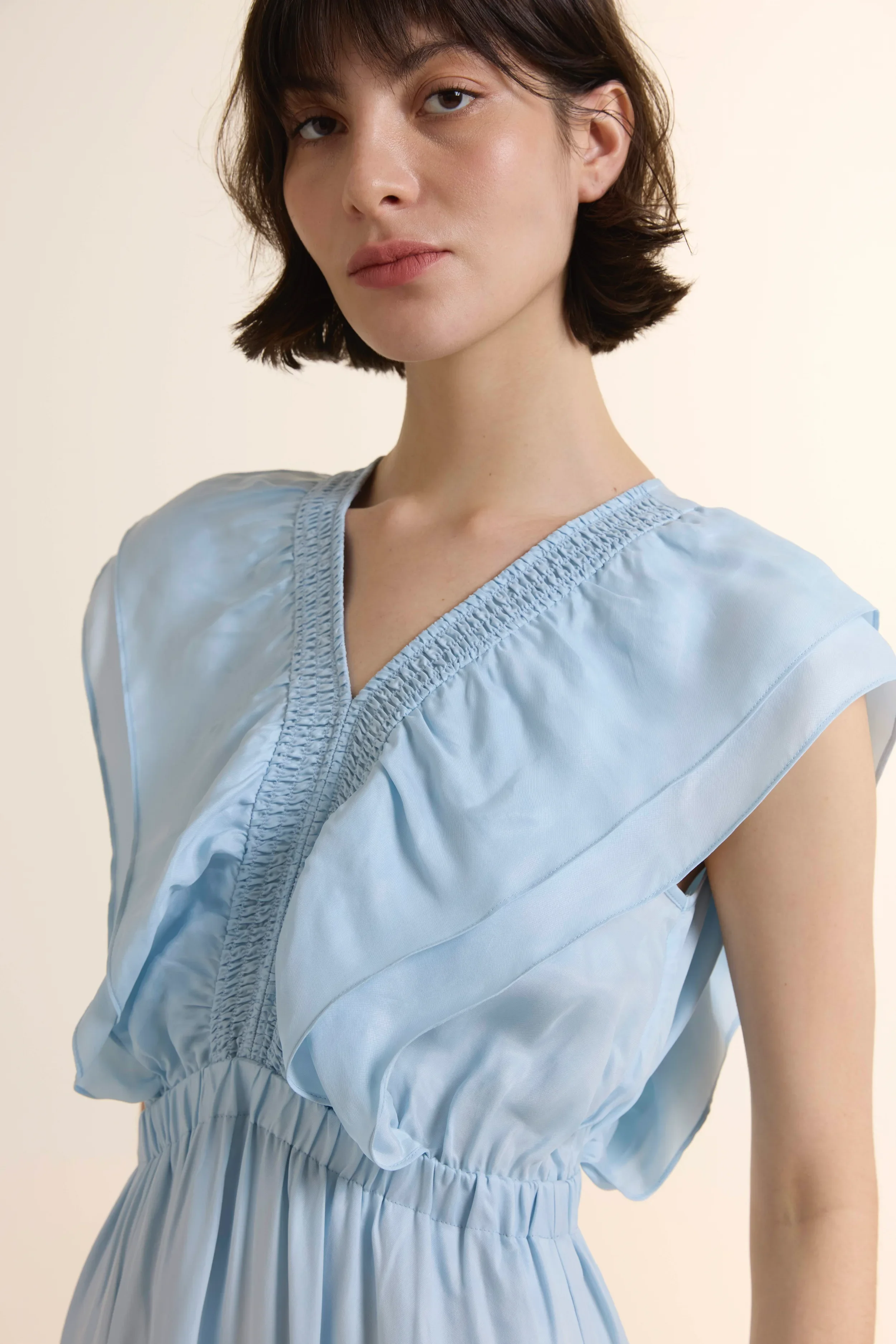 Full-length photo of a model in the Azure Fluid Flounce Midi Dress, featuring a tiered skirt, ruffle V-neckline, and elastic waist, crafted from a sustainable Cupro and Viscose blend.