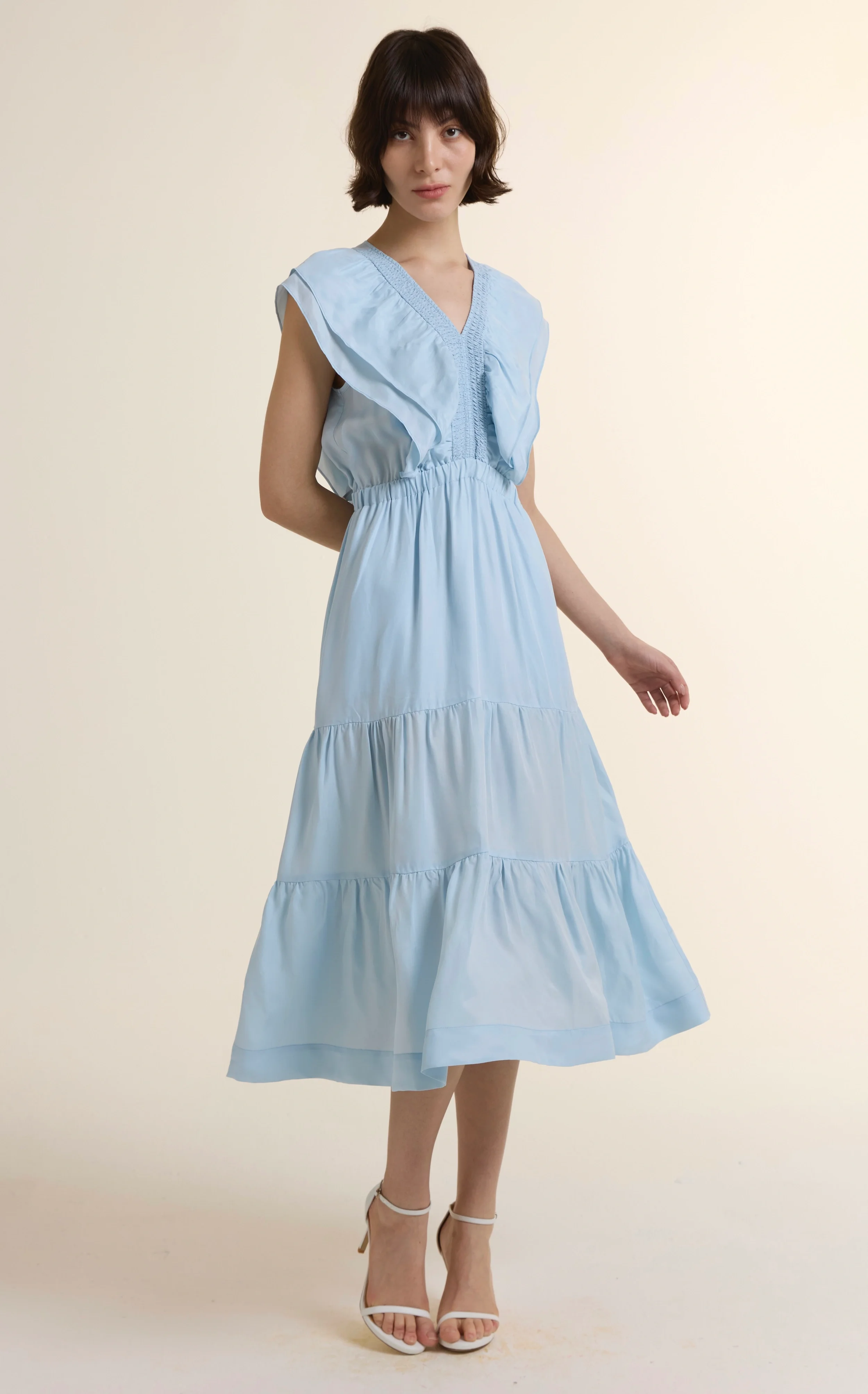 Full-length photo of a model in the Azure Fluid Flounce Midi Dress, featuring a tiered skirt, ruffle V-neckline, and elastic waist, crafted from a sustainable Cupro and Viscose blend.