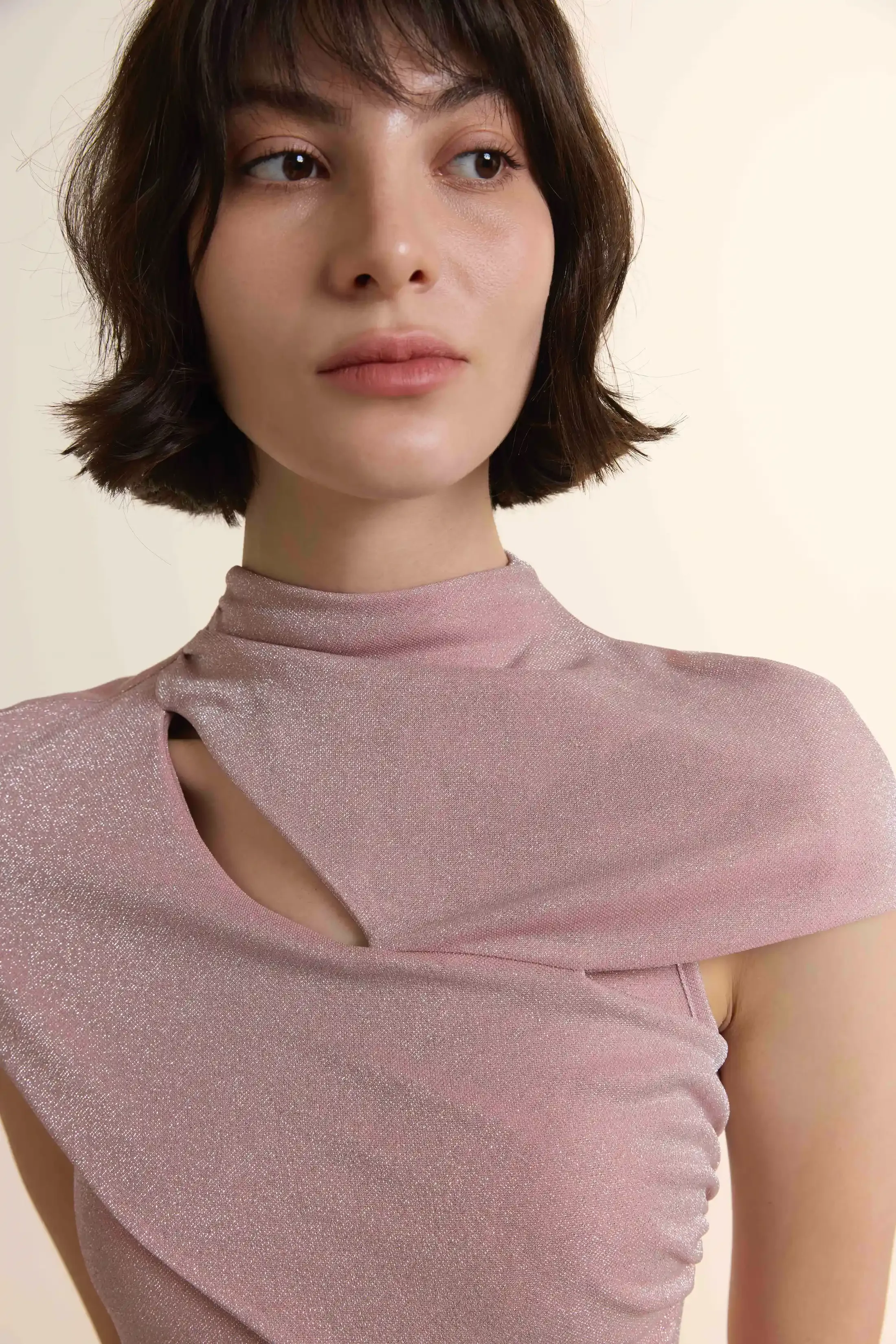 A close-up shot of the Luminous Pleated Maxi Gown, highlighting the intricate sculptural wrap detailing at the bodice and the subtle metallic shimmer of the pleated fabric. The design includes a contemporary mock neck with an elegant cutout effect.