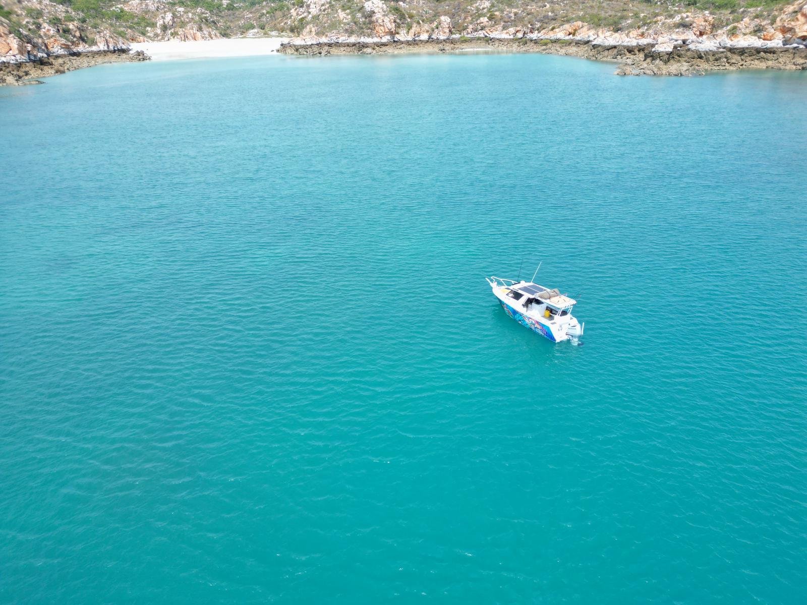 A boat floating on a large, calm body of turquoise water near rocky shores with sparse vegetation.