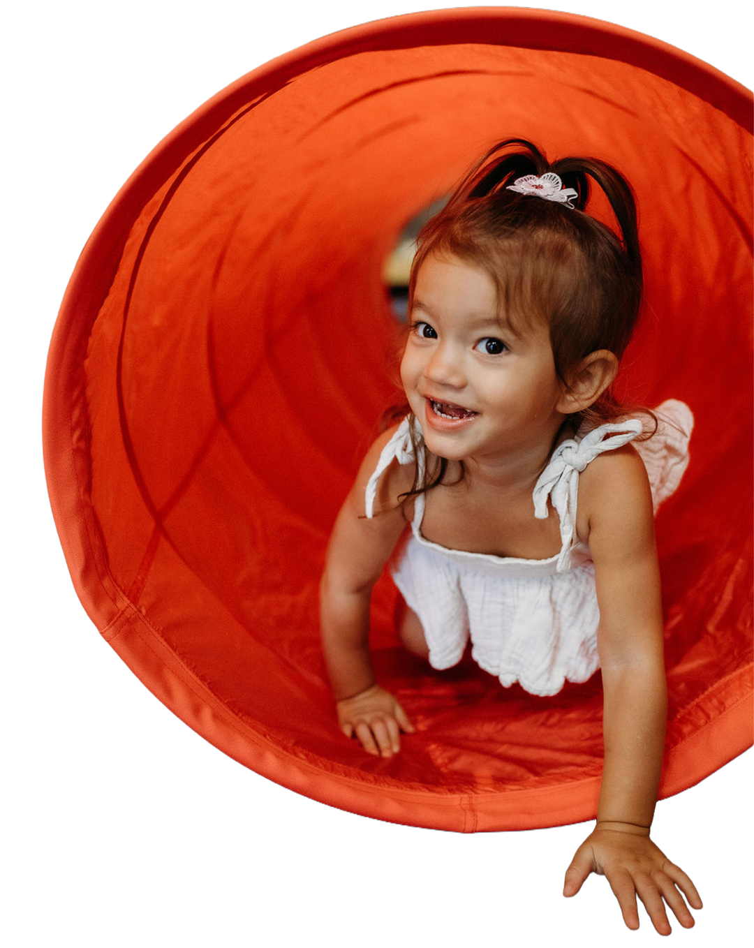 Young girl with brown hair and a white dress crawling through an orange tunnel