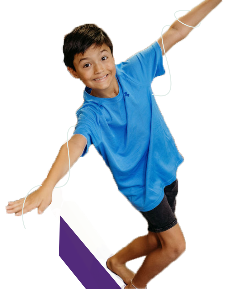 Smiling boy in blue t-shirt and dark shorts balancing on a skateboard.