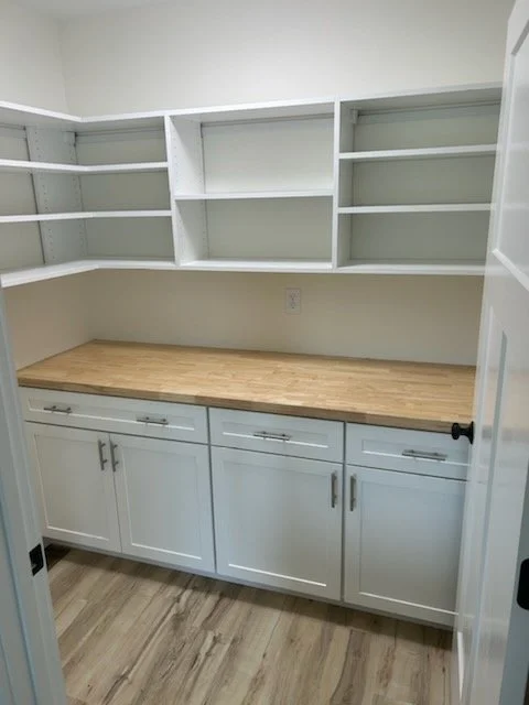 Empty white kitchen or pantry cabinets with open shelves and a wooden countertop.