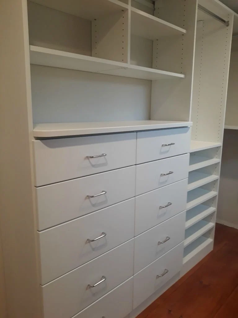 White built-in closet with multiple drawers, open shelving, and hanging rods for storage.