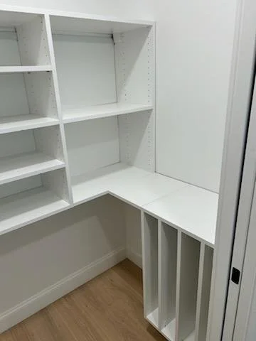 Empty white built-in closet with shelves and storage compartments in a room corner.