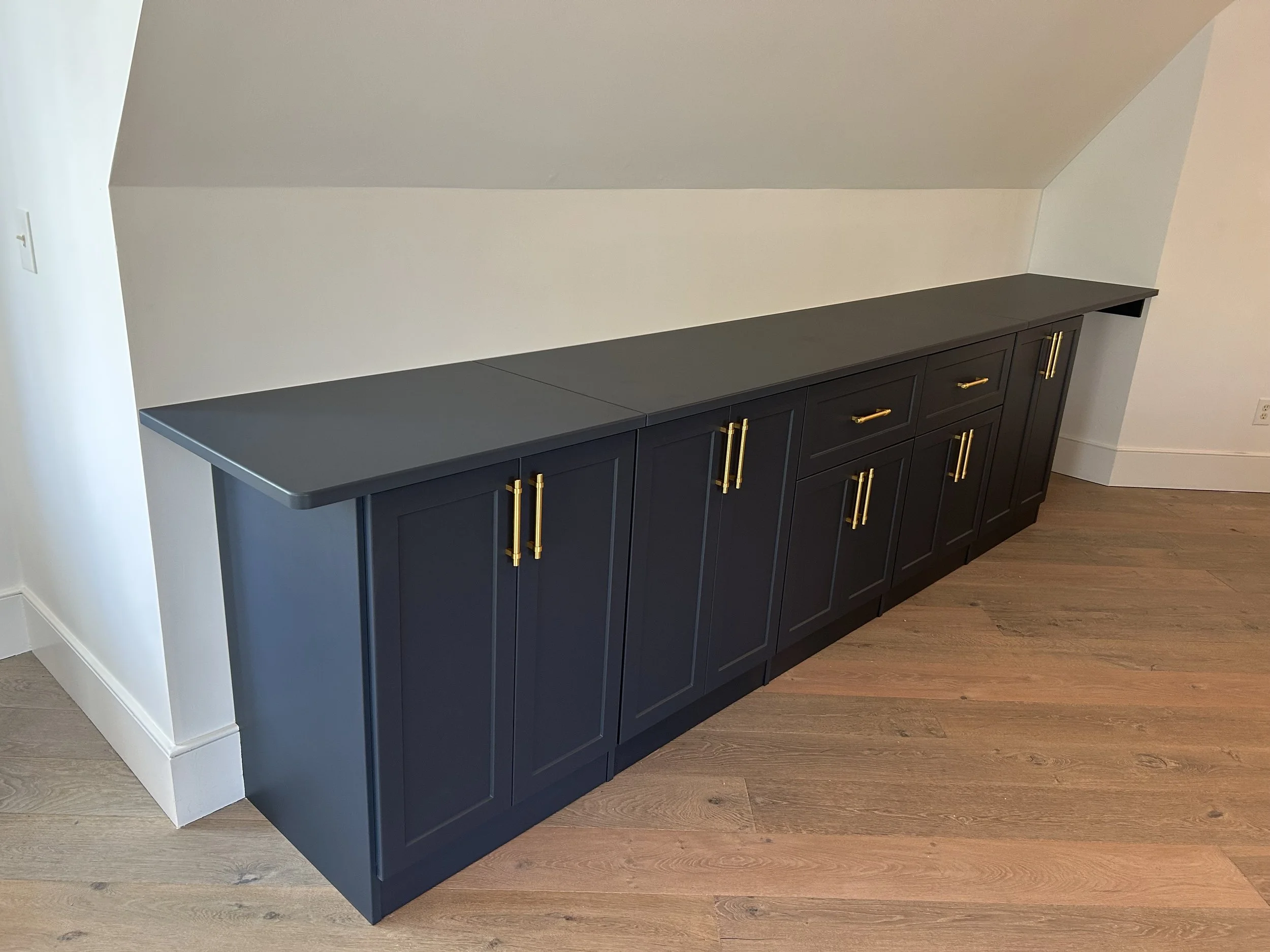 Dark blue sideboard with gold handles placed against a white wall in a room with wooden flooring.