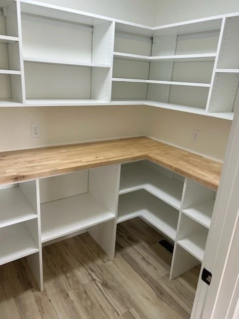 Empty white built-in shelves with a wooden countertop in an interior room with hardwood flooring.