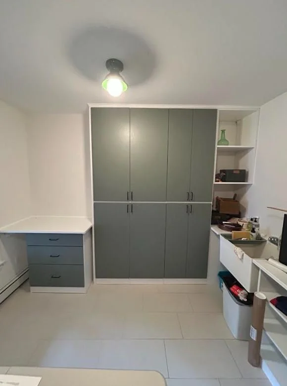 A room with a grey closet, a small blue dresser, and built-in shelves with various items, under a ceiling light.