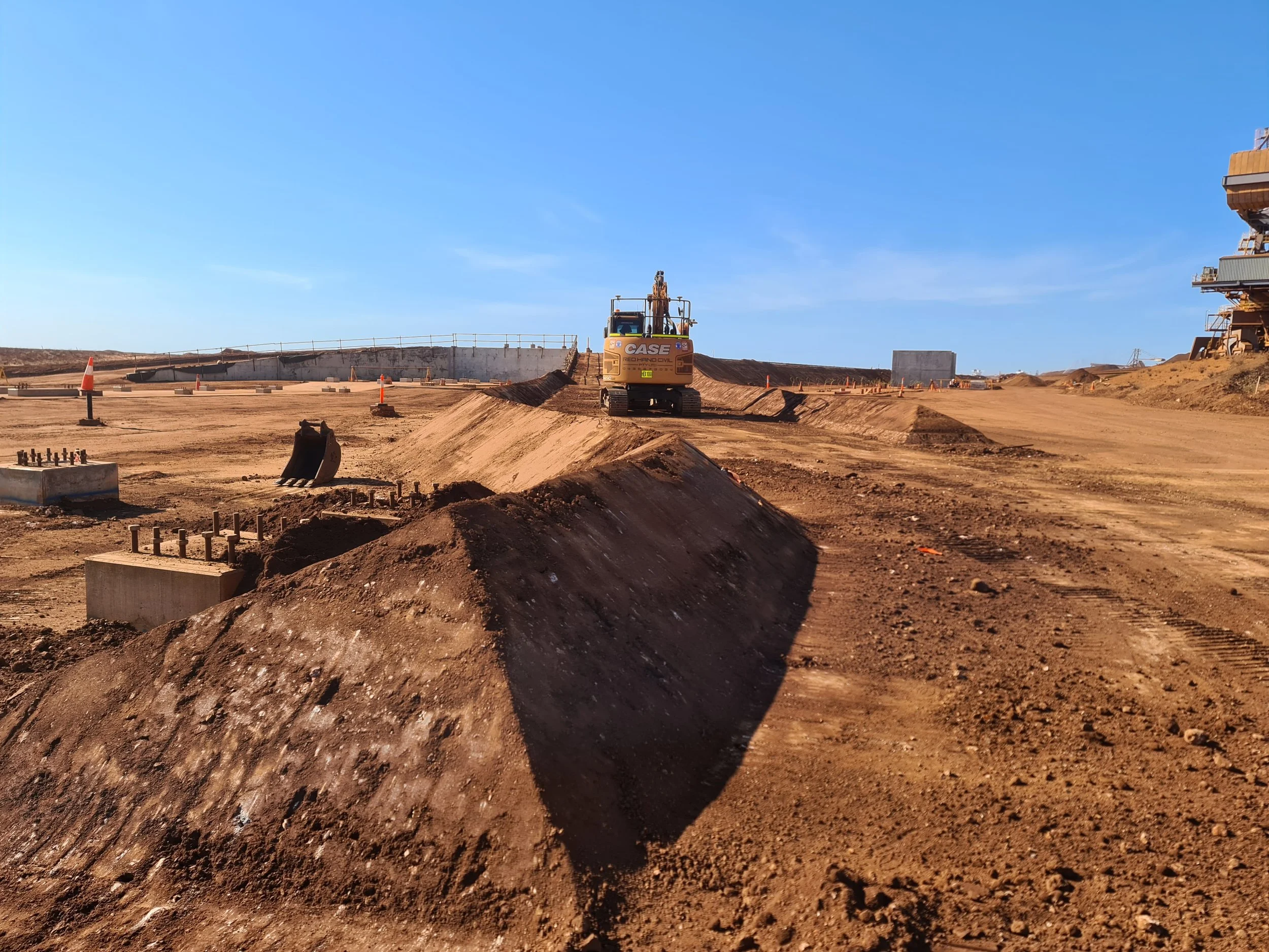 Construction site with dirt mounds, construction equipment, and a clear blue sky.