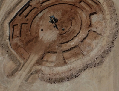 Aerial view of an excavated circular construction site with heavy machinery working on the site.