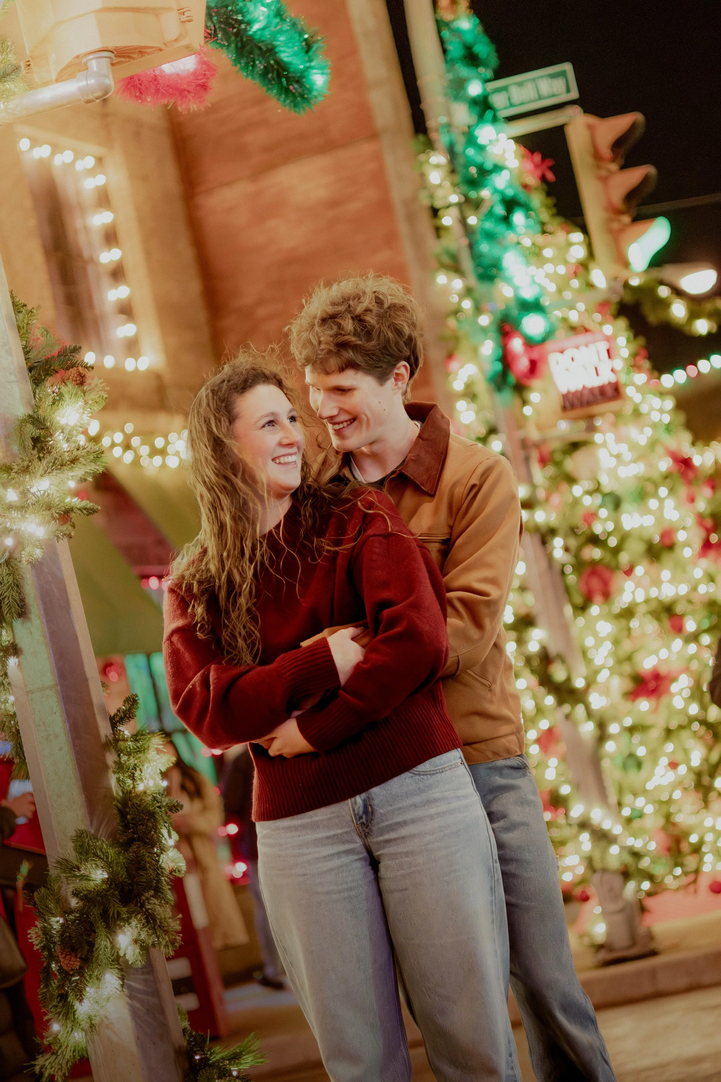 A young couple dancing and smiling at a Christmas market decorated with lights and ornaments