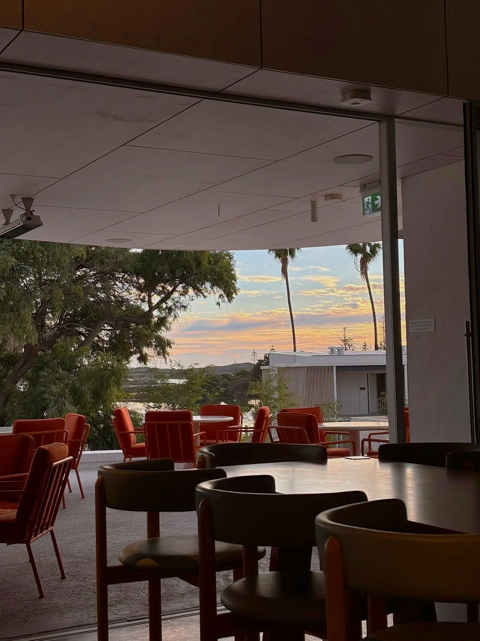 Interior seating area at sunset with orange chairs and views of trees, water, and palm trees outside.