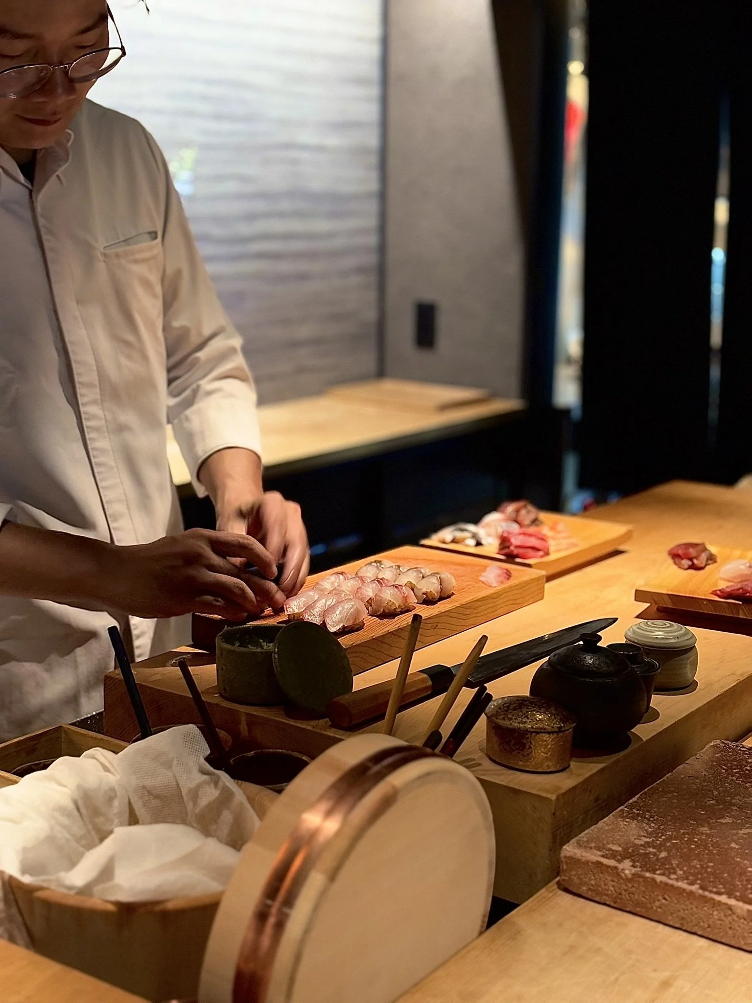 A chef preparing sushi at a wooden counter in a restaurant with dim lighting.