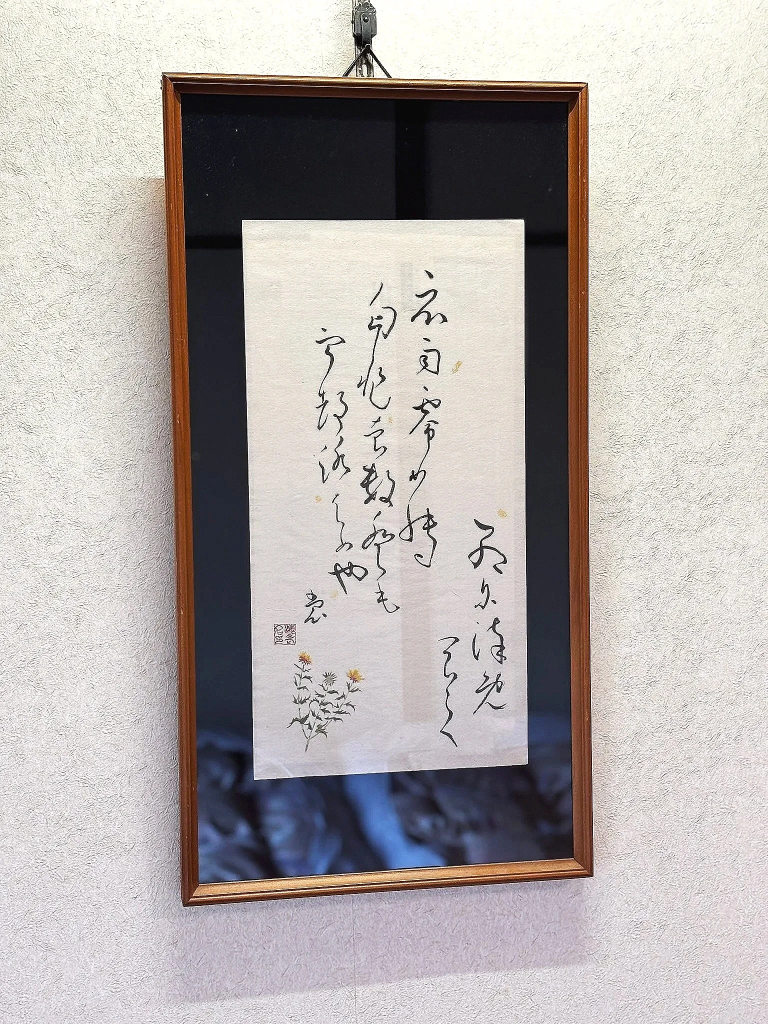 Japanese calligraphy on a hanging scroll with a drawing of flowers at the bottom.