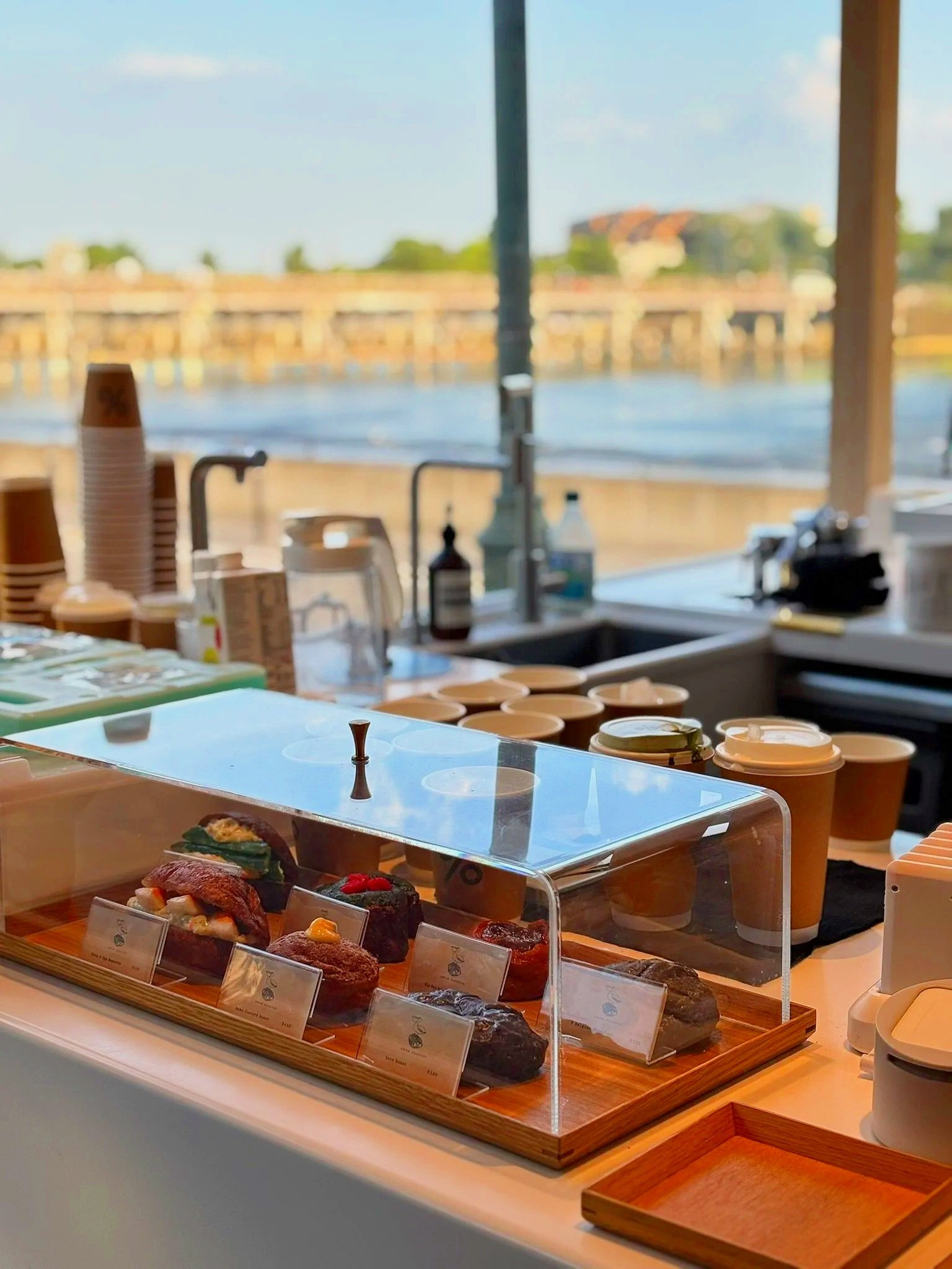 Display of assorted pastries and desserts in a bakery case near a window with a river view
