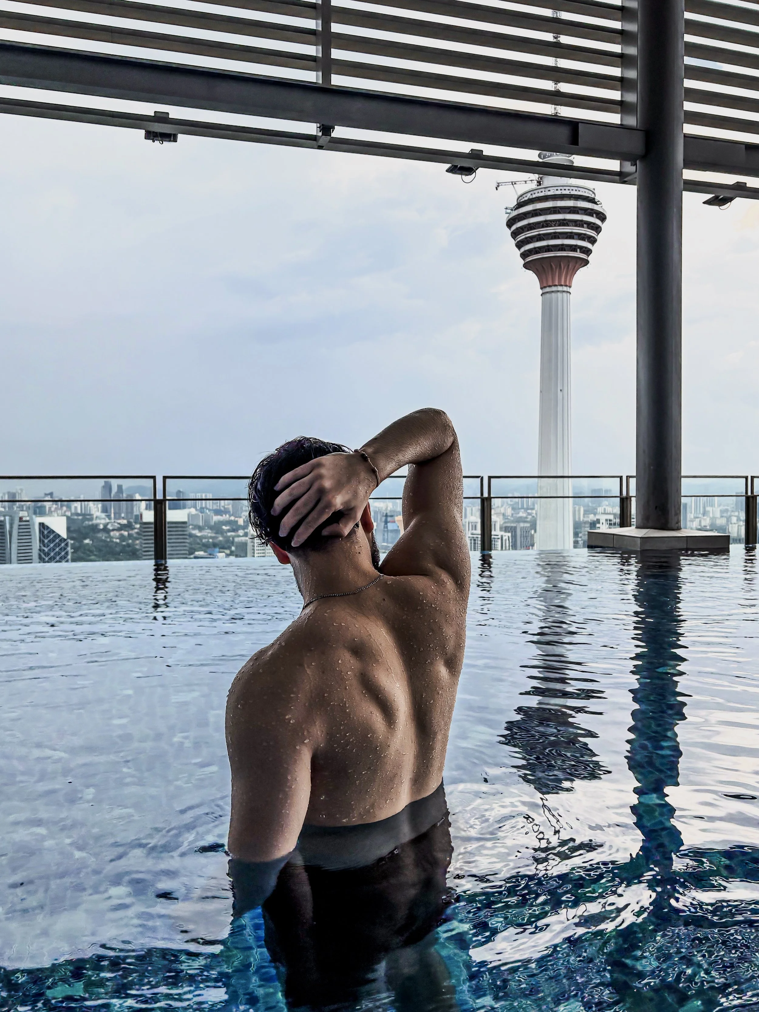 A man in an infinity pool with city skyline and a tall tower in the background.