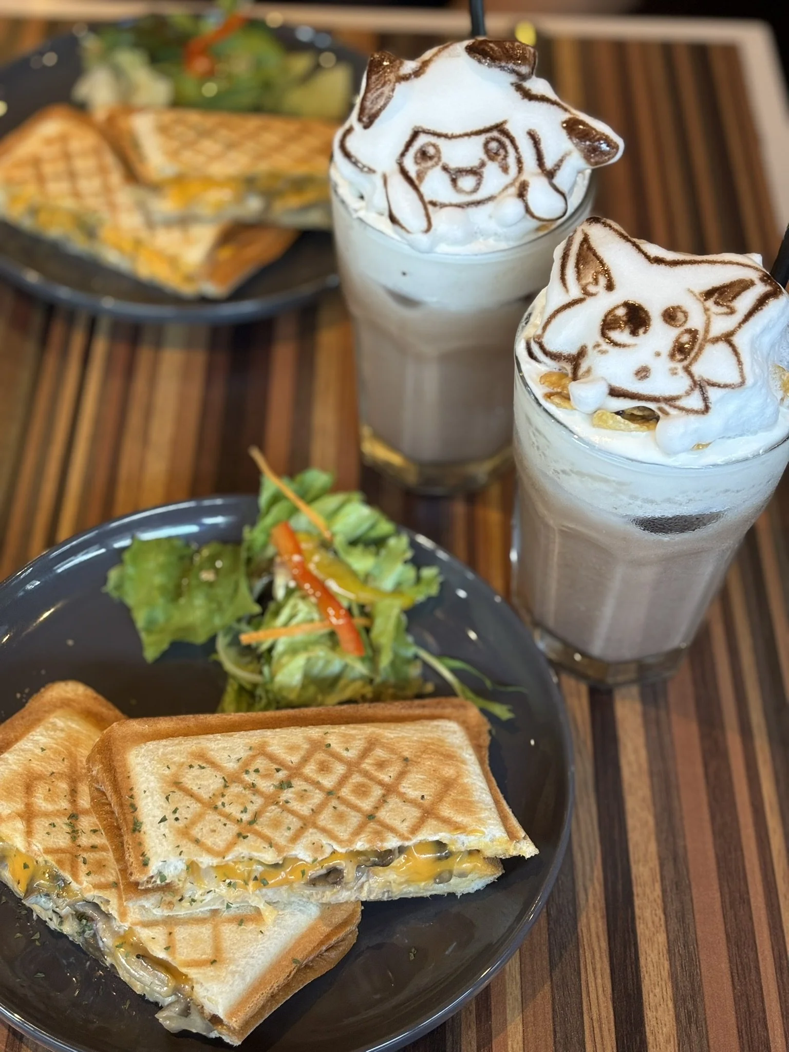 A meal with a grilled cheese sandwich, a side salad, and two milkshakes topped with whipped cream and edible art of cartoon characters.