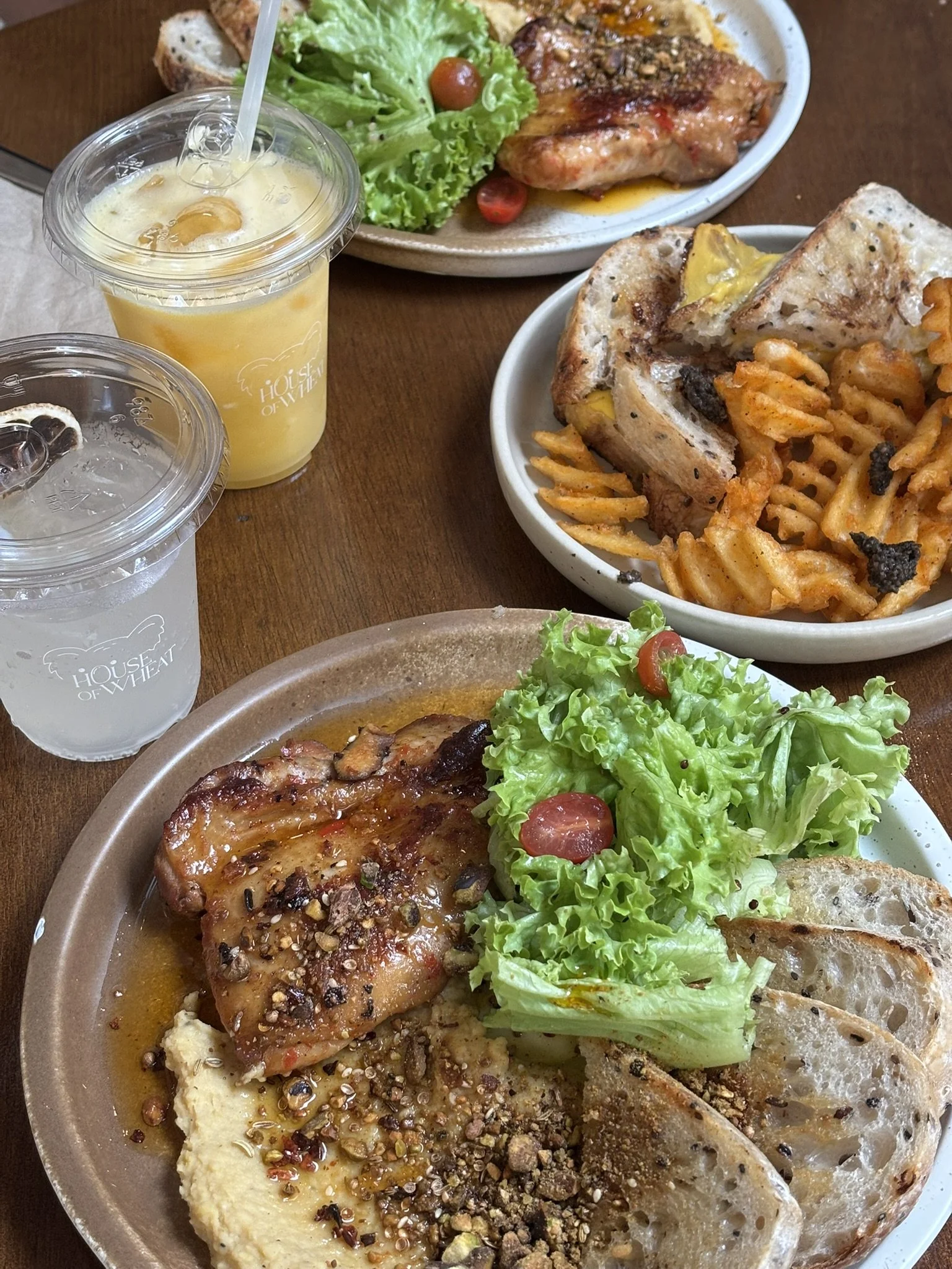 A spread of Mediterranean-style dishes including grilled chicken with salad, pasta with sauce, hummus with bread, and a plate with a piece of chicken, salad, and bread slices, accompanied by two cups of refreshing beverages.