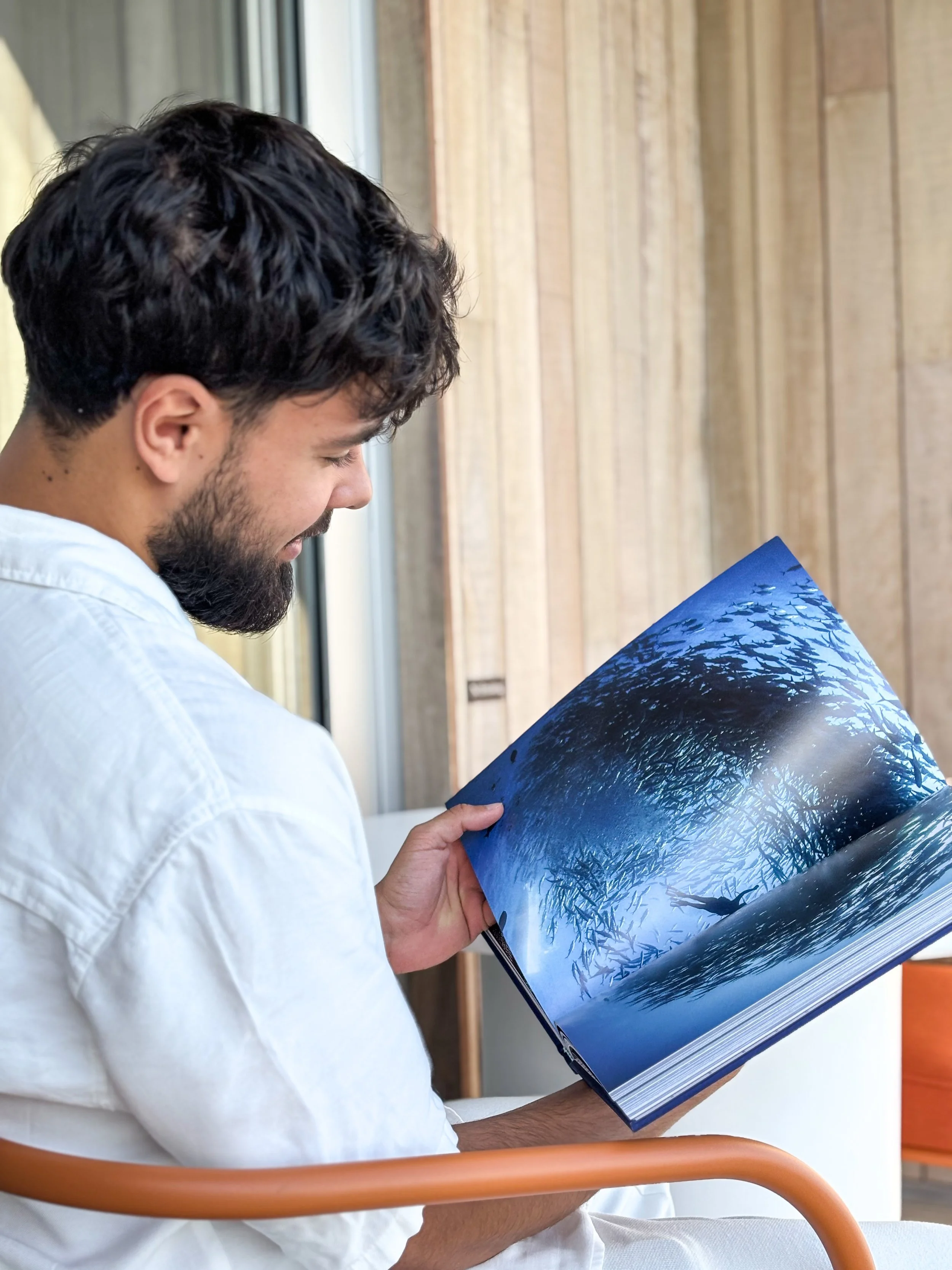 A man with dark curly hair and a beard looking at a large book with a blue-colored image of a lake and trees.