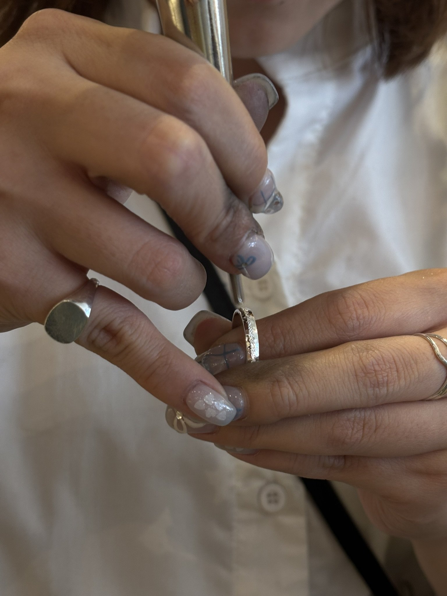 A person is holding a ring and using a tool to perform a procedure on their finger, with detailed nail art visible.