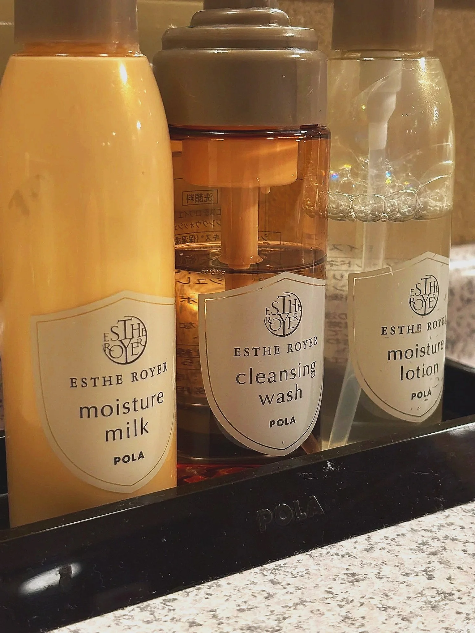 Set of three skincare bottles labeled Moisture Milk, Cleansing Wash, and Moisture Lotion from Esther Royer by Pola on a black tray.