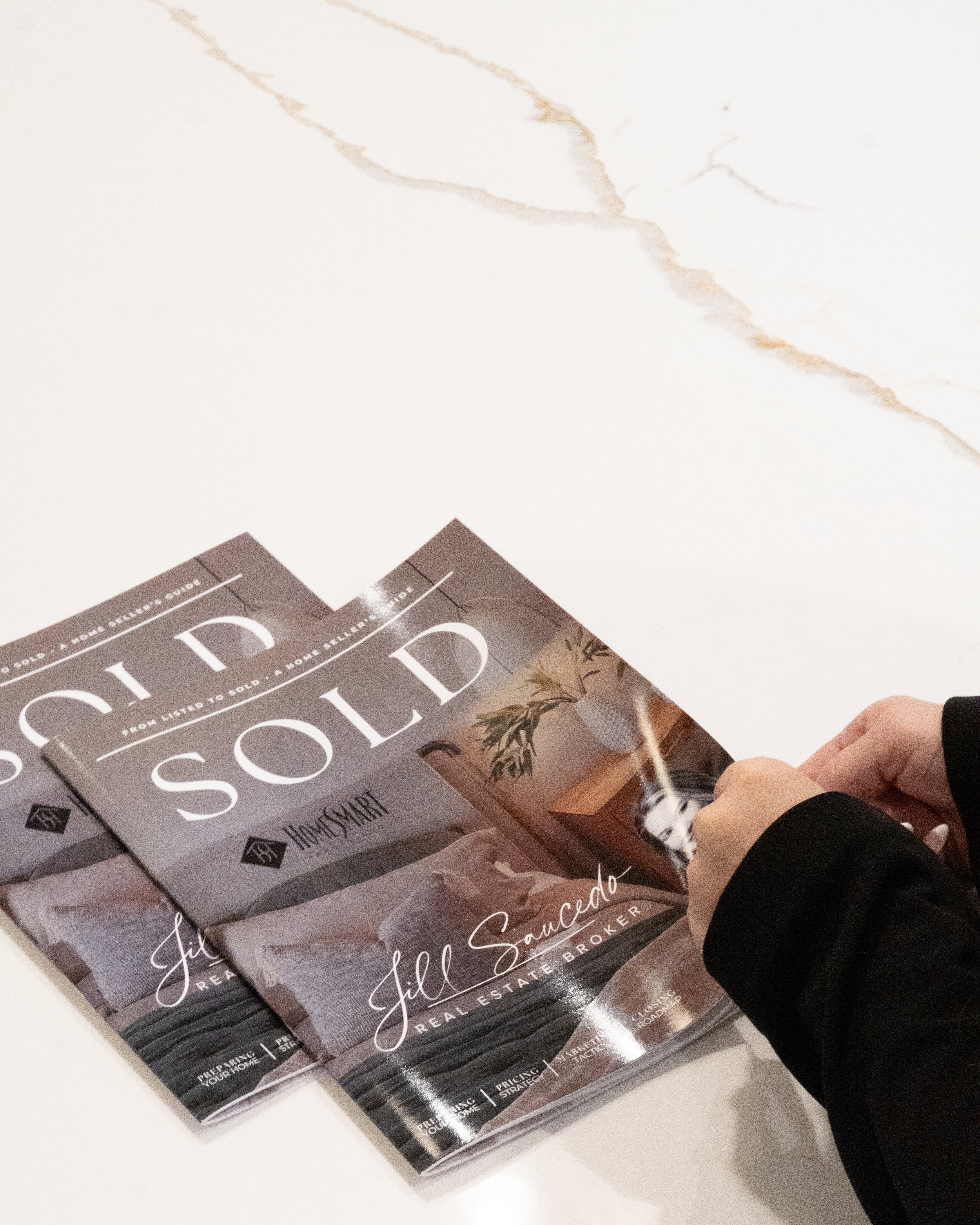 Portland metro real estate agent, Two real estate magazines on a white surface with a hand holding one magazine.