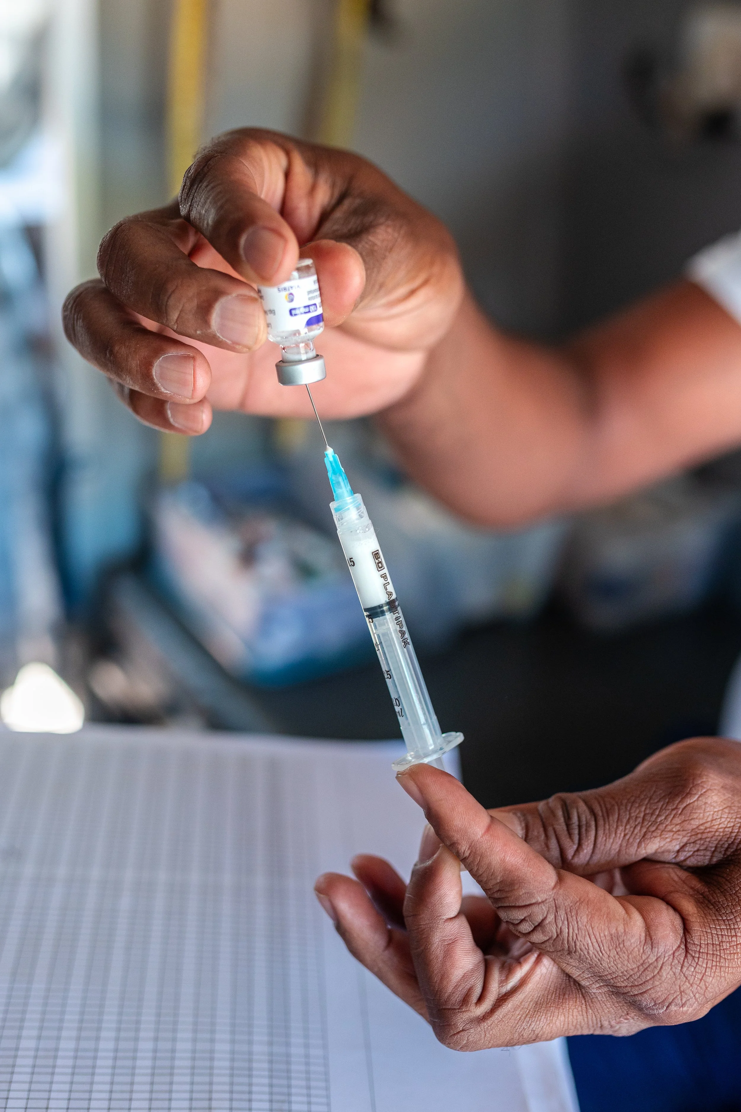 Close-up of a person drawing a liquid vaccine into a syringe using a small vaccine vial, with hands and syringe in focus.