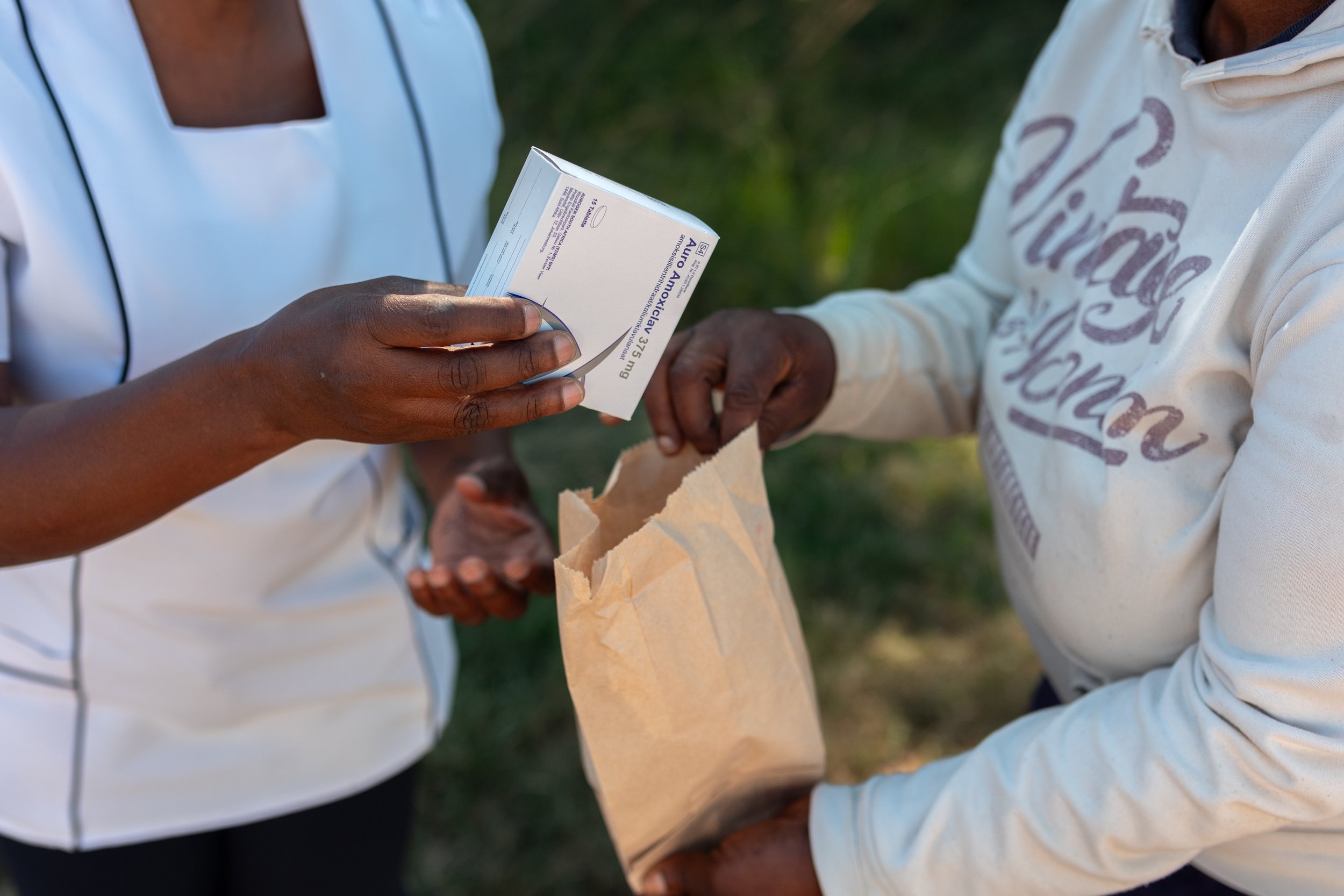 Two people exchanging medication and a paper bag in an outdoor setting.