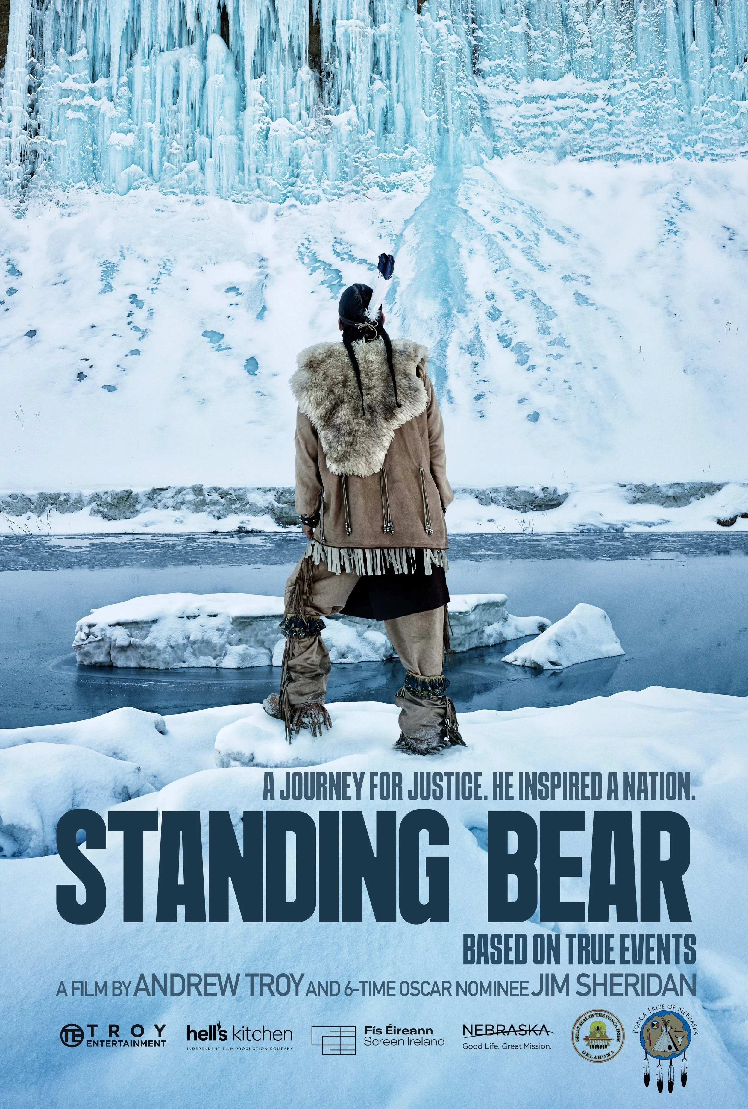 Poster for the narrative feature film 'Standing Bear' depicting a person in traditional Native American attire standing by a frozen lake with ice cliffs behind, emphasizing themes of justice and inspiration from true events.