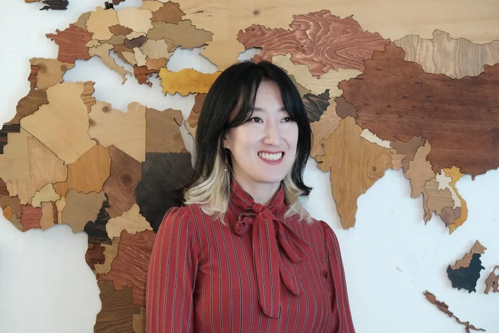 A woman smiling in front of a wooden map of Asia.