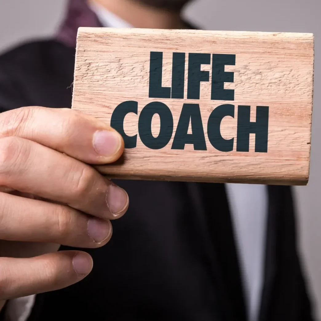 A person holding a wooden sign that says 'Life Coach' in bold black letters.