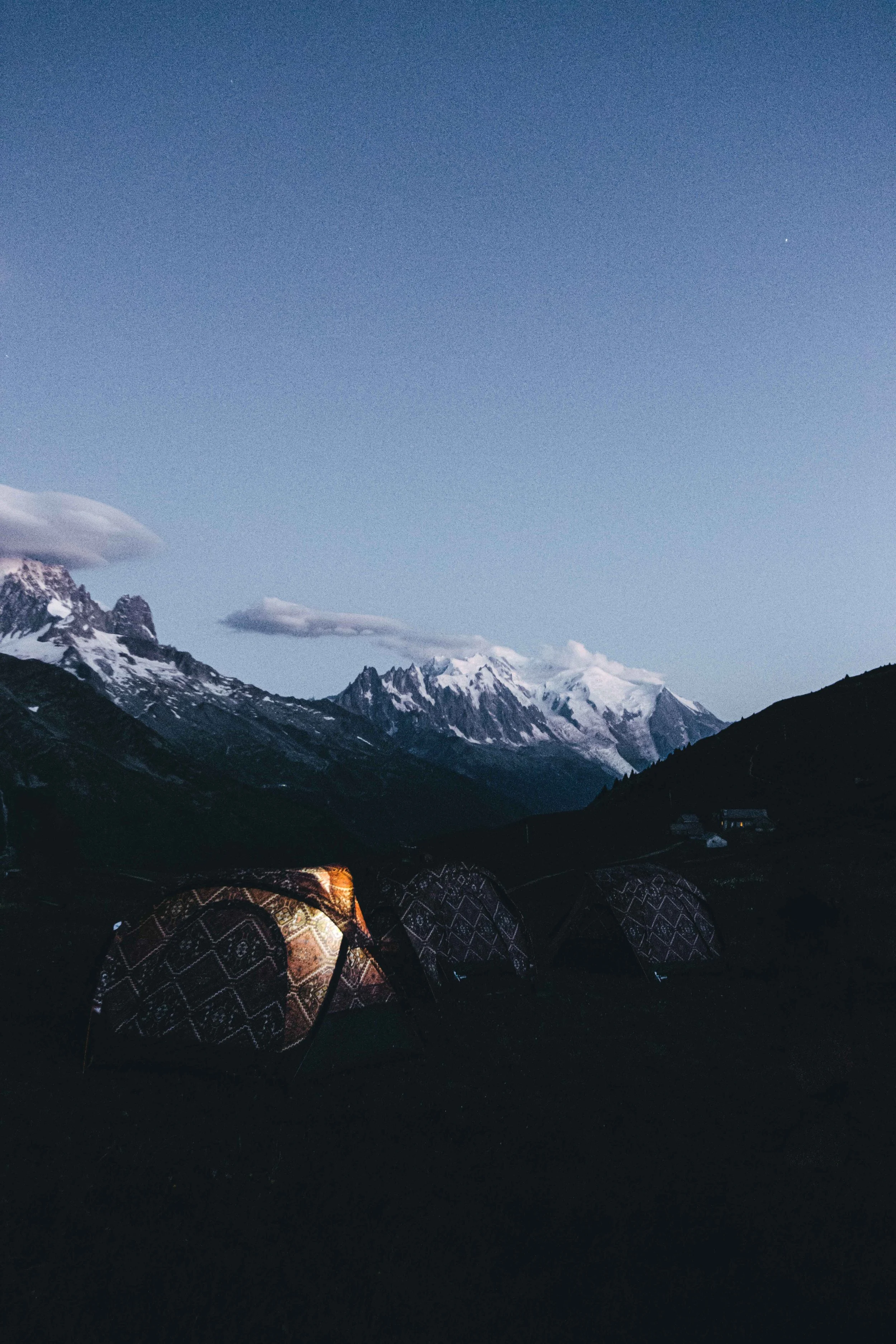 Tentes décoratives dans un paysage de montagnes enneigées au coucher du soleil, sous un ciel clair.