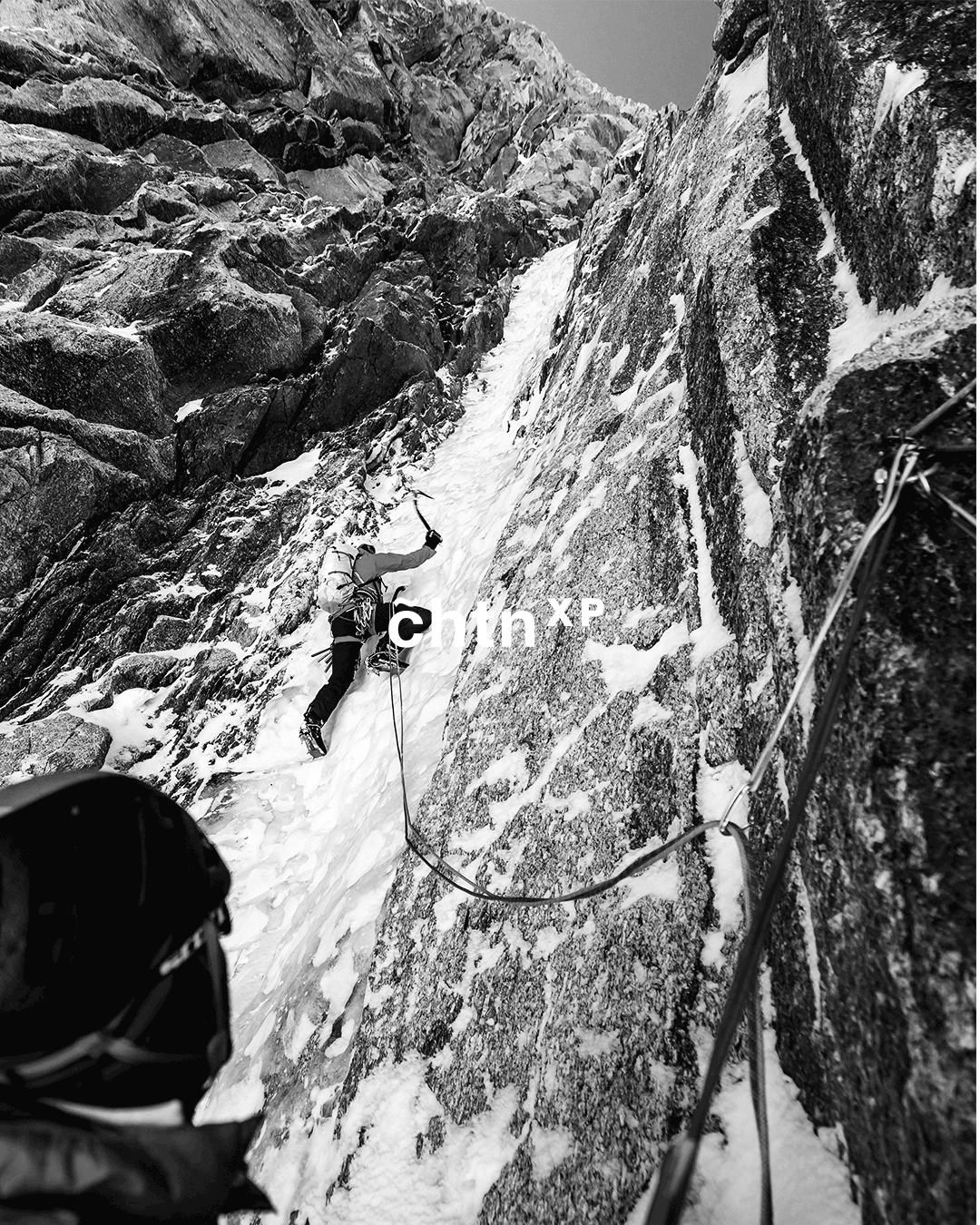 Un alpiniste escalade une falaise enneigée dans un environnement rocheux.